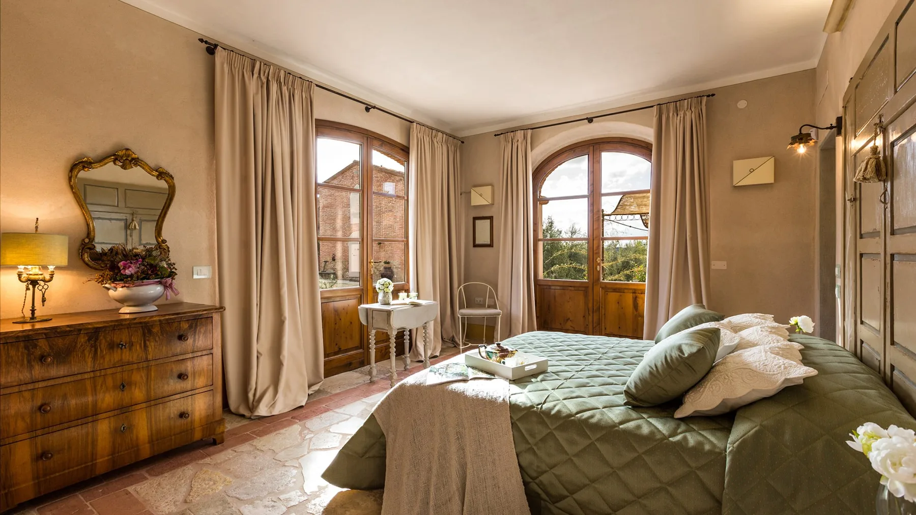 A bedroom with a large bed, wooden doors, and tall windows.