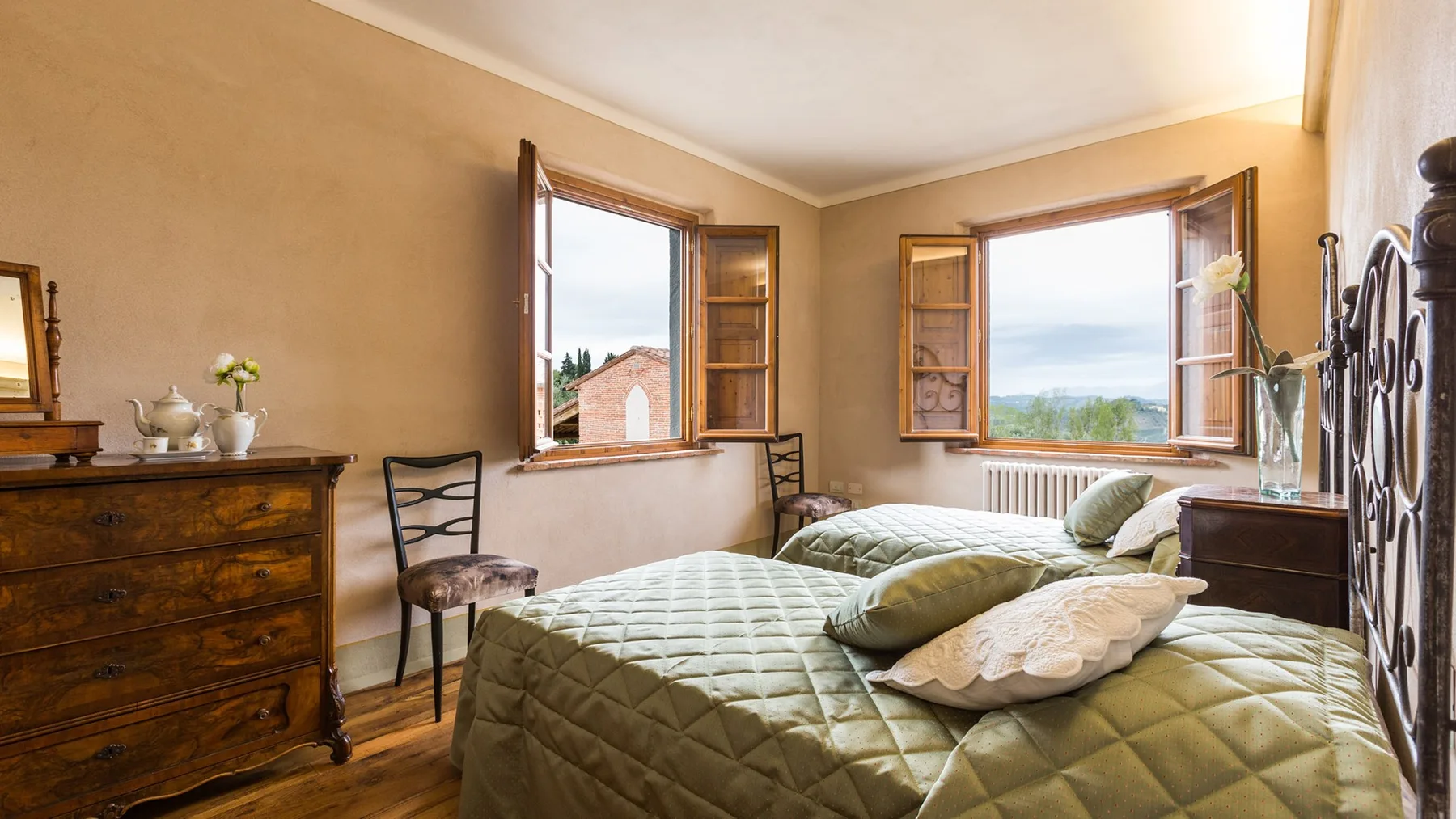 A bedroom with two beds beside open windows overlooking the landscape.