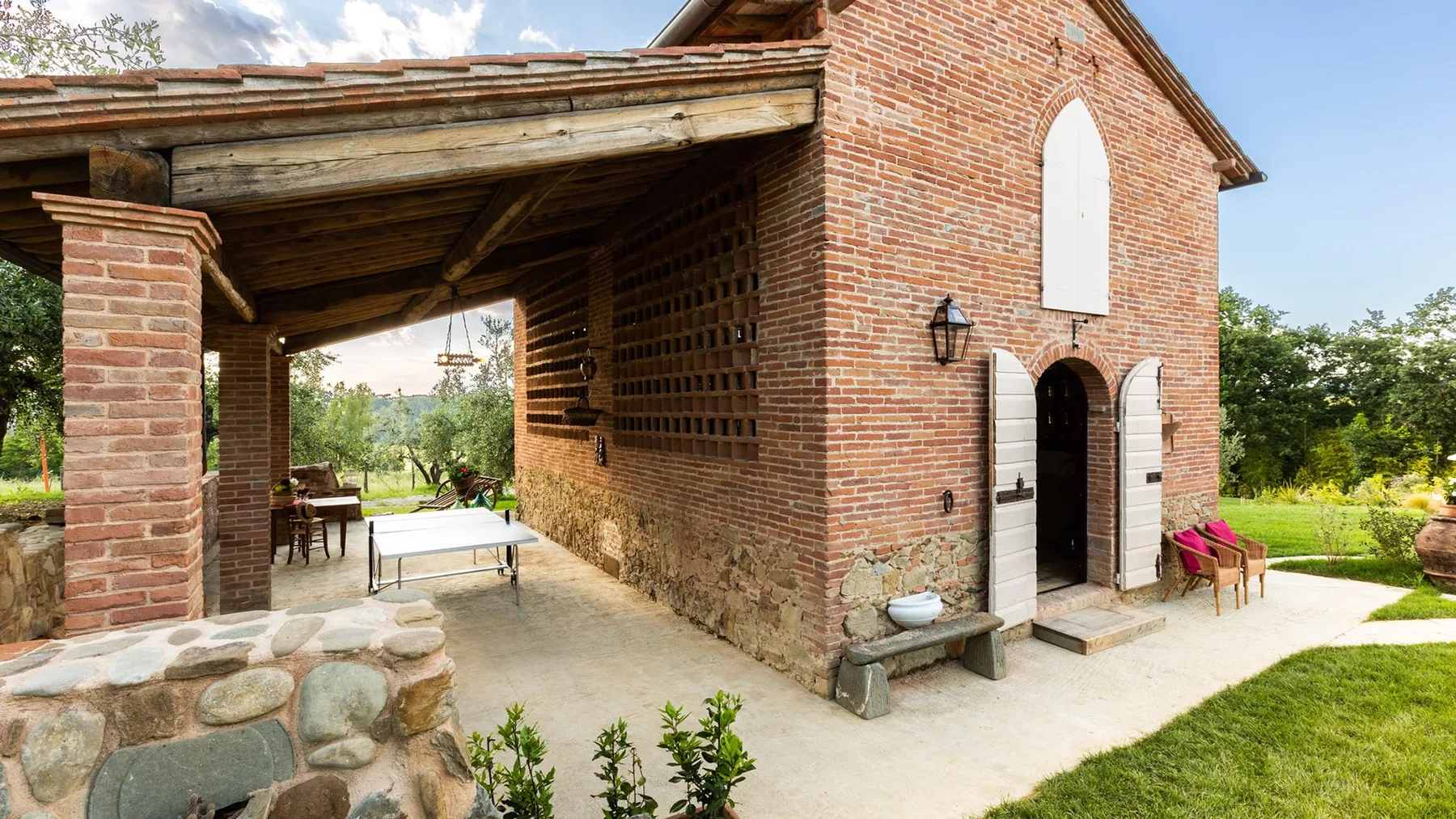 A brick building with a covered outdoor seating area beside a grassy yard.