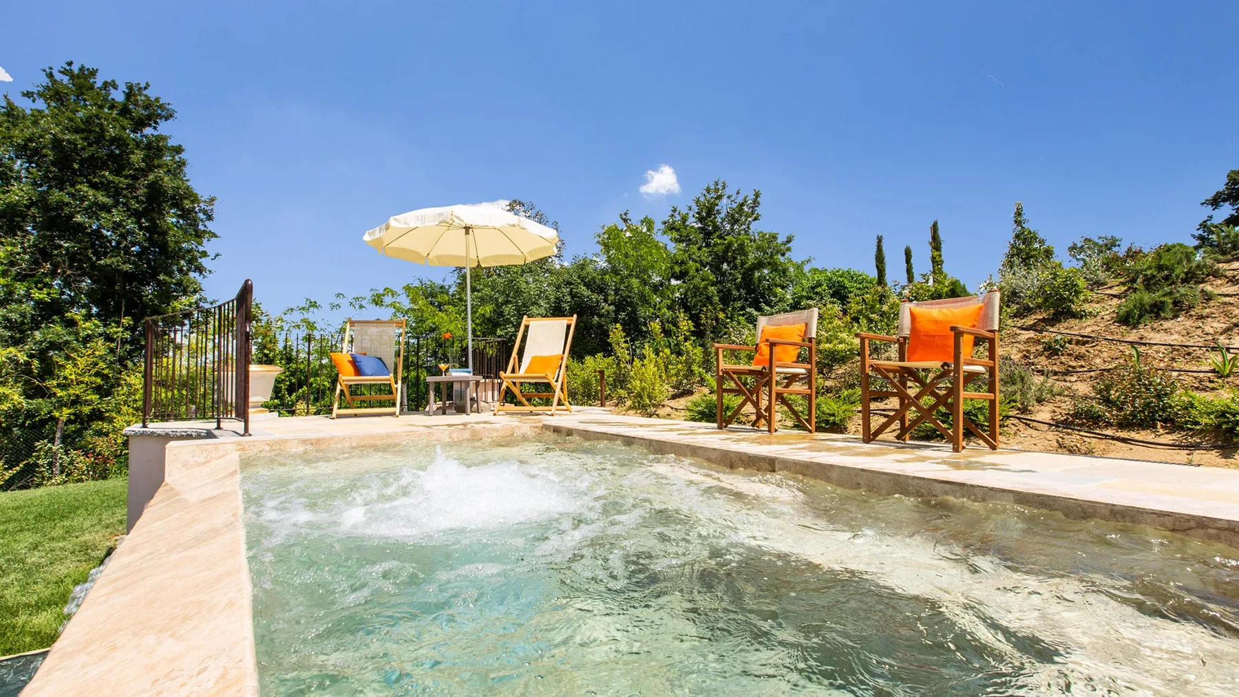An outdoor swimming pool with seating and an umbrella beside the water.
