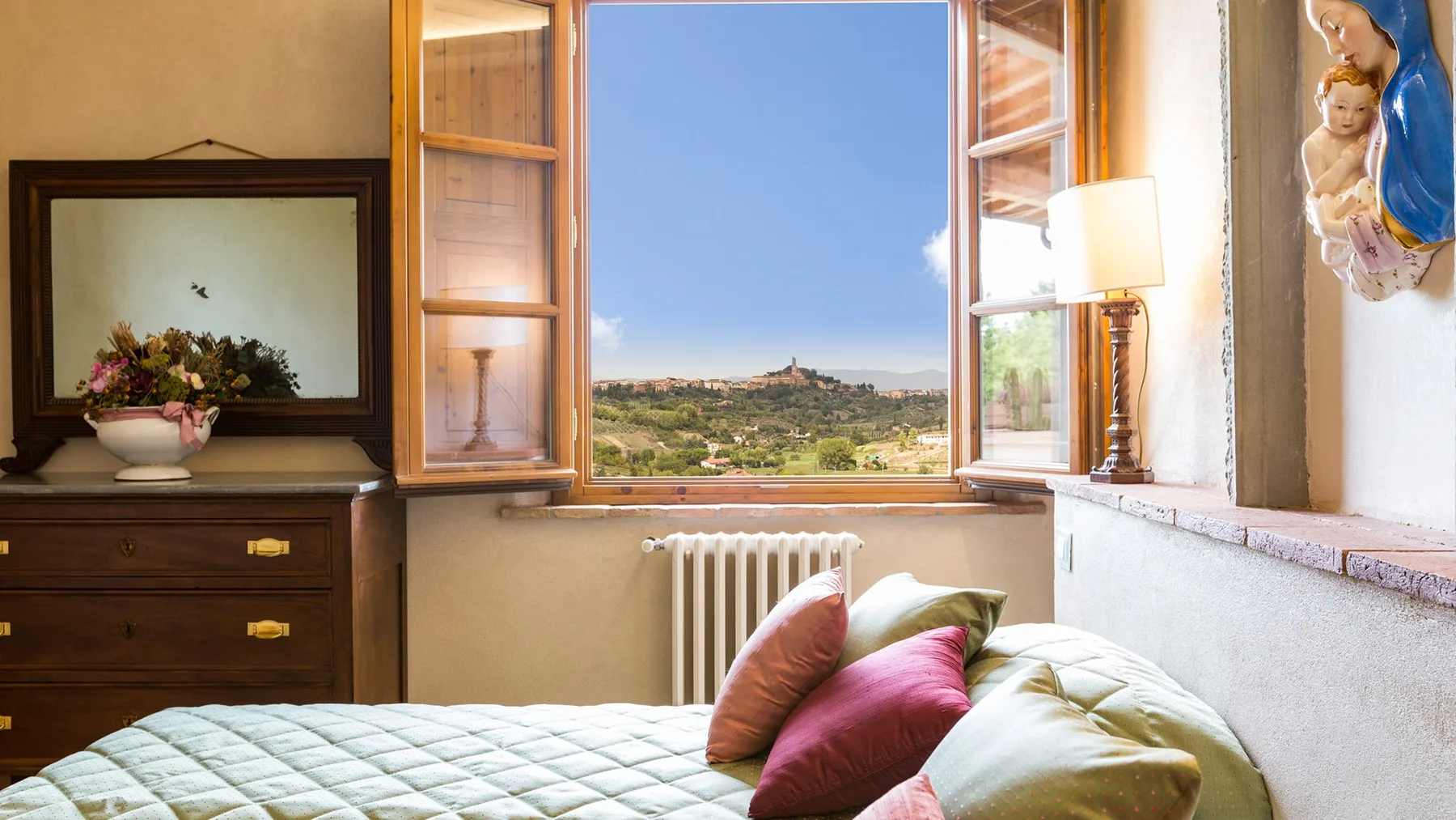 A bedroom with an open window overlooking a green landscape.