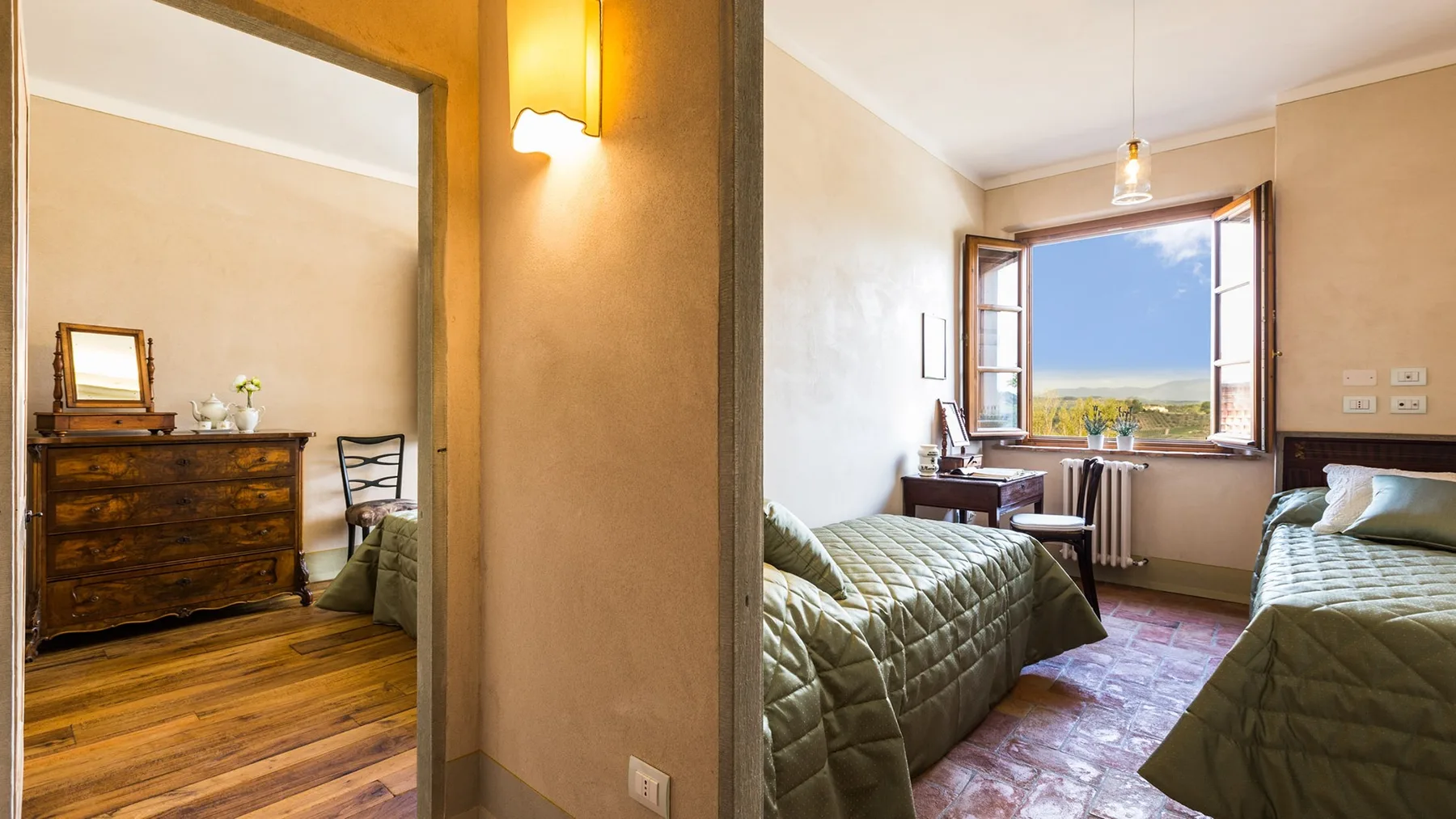 A bedroom with two beds, an open window, and a dresser in the adjoining area.