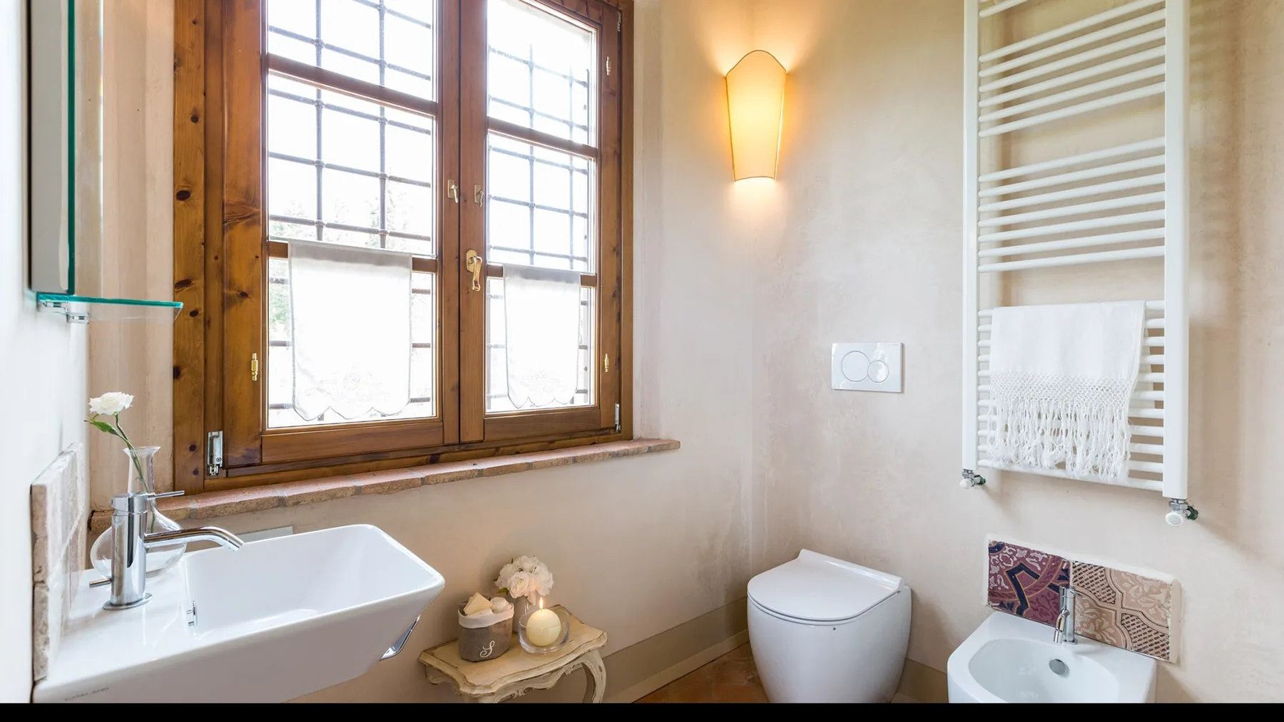 A bright bathroom with a wooden-framed window, sink, toilet, and towel warmer.