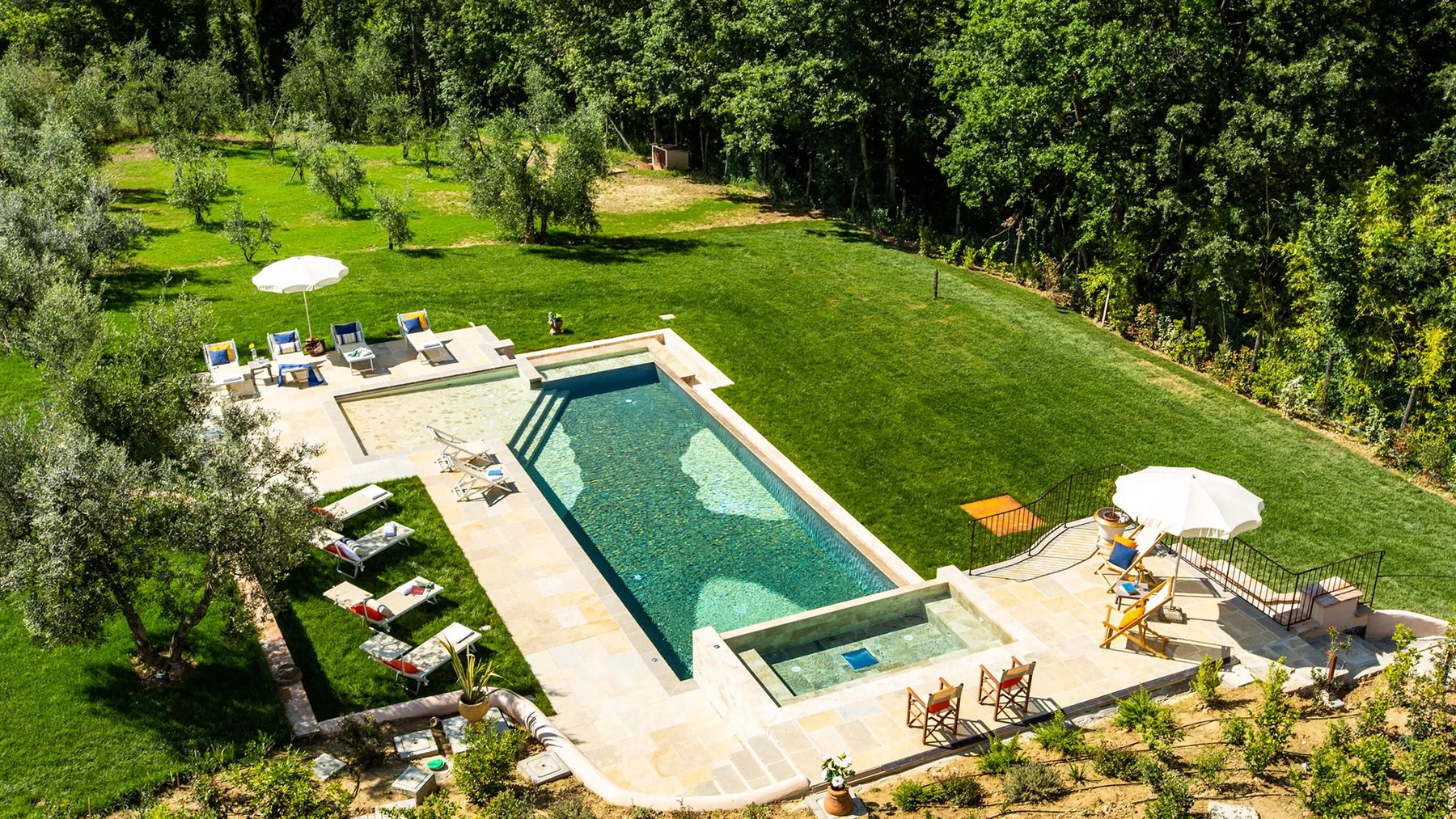 A swimming pool and paved patio sit in a broad green garden.