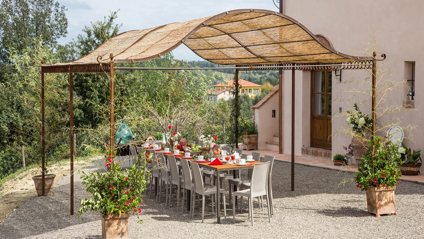 An outdoor dining area sits beneath a woven canopy, with plants around the table.