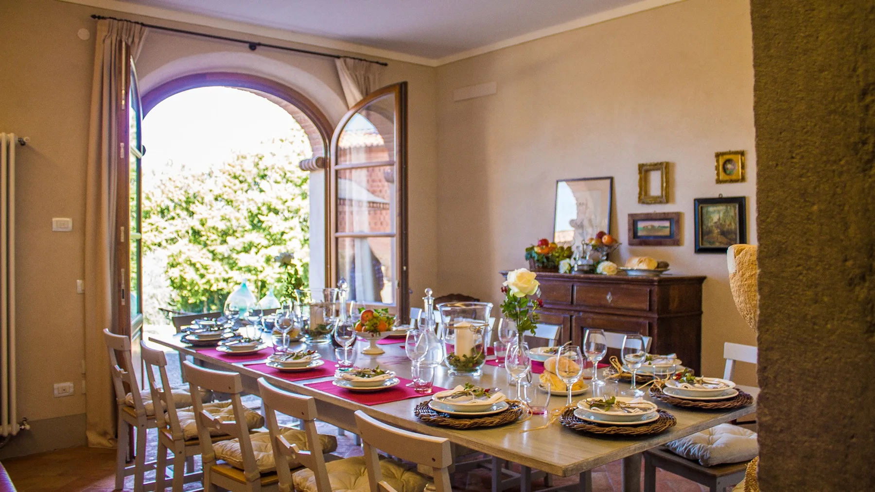 A dining room with a long set table beside an open arched window.