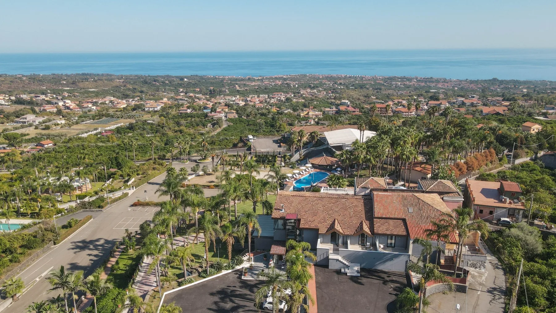 Vista aérea de un barrio costero con casas, palmeras y el mar al fondo.
