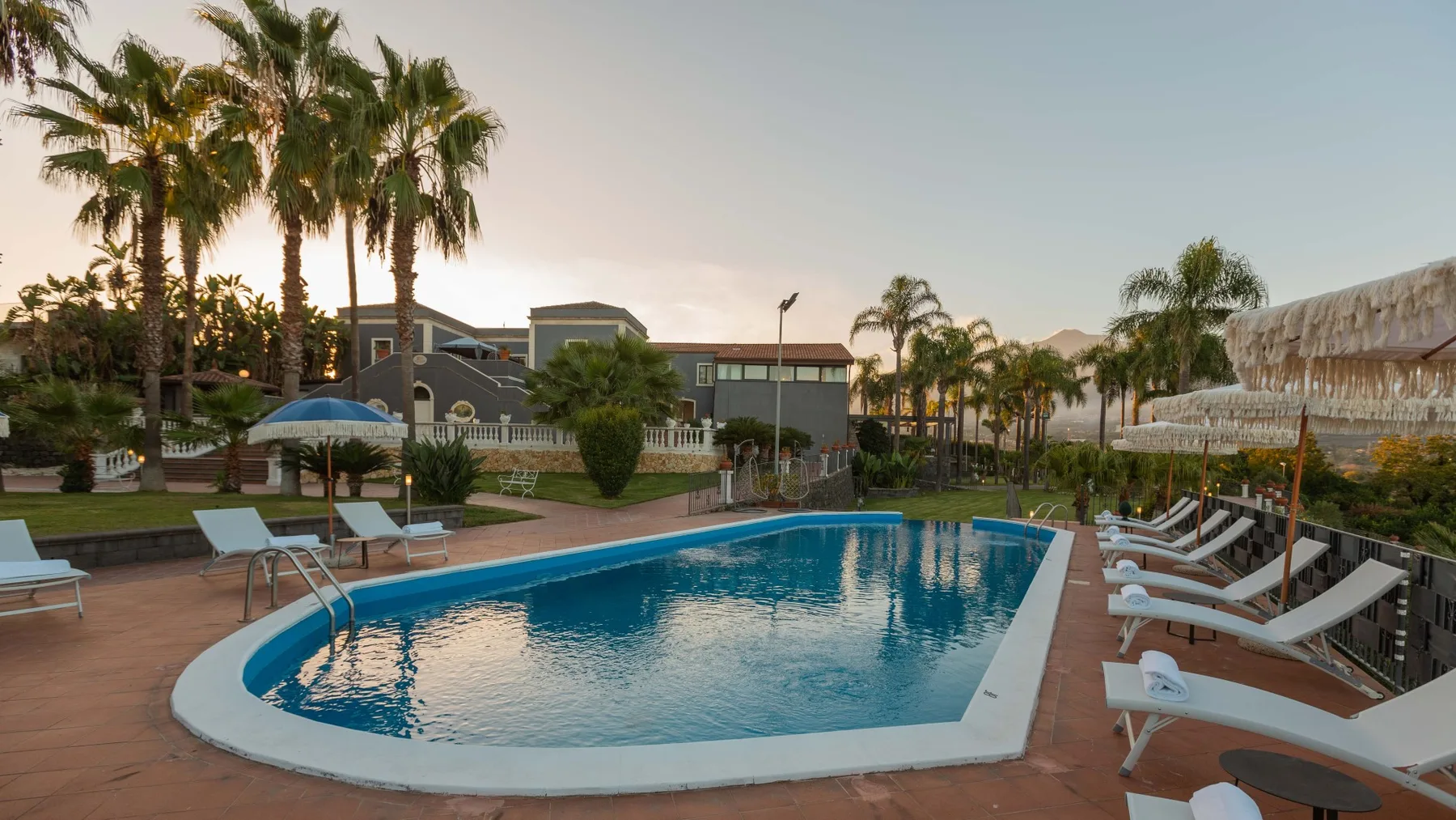 Una piscina al aire libre está rodeada de tumbonas y palmeras.