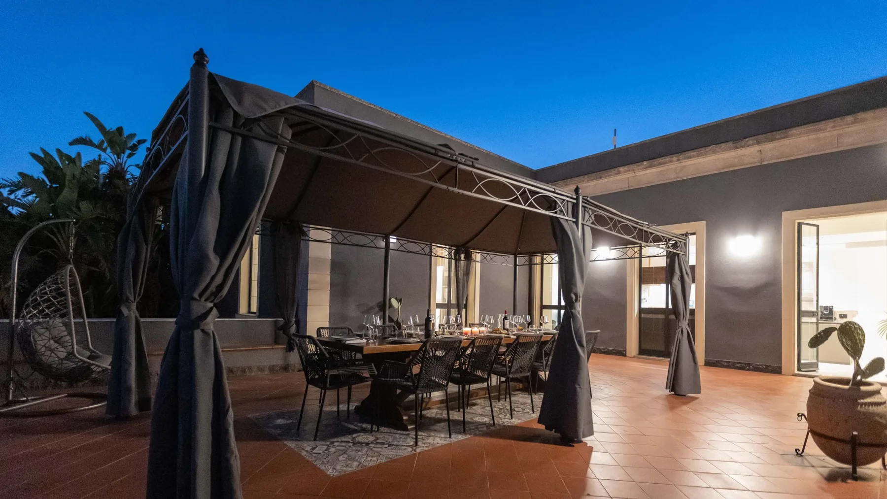 Comedor exterior cubierto con una mesa y asientos junto a un edificio moderno.