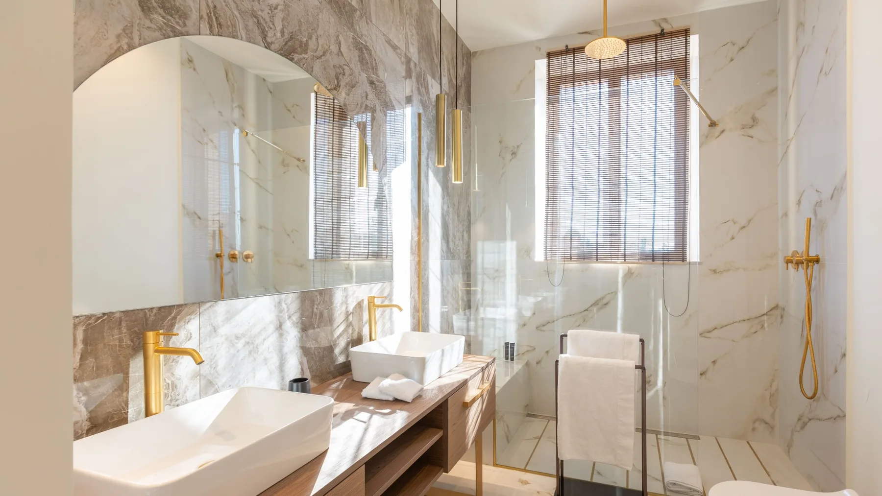 Un baño luminoso de mármol con ducha de vidrio y tocador.