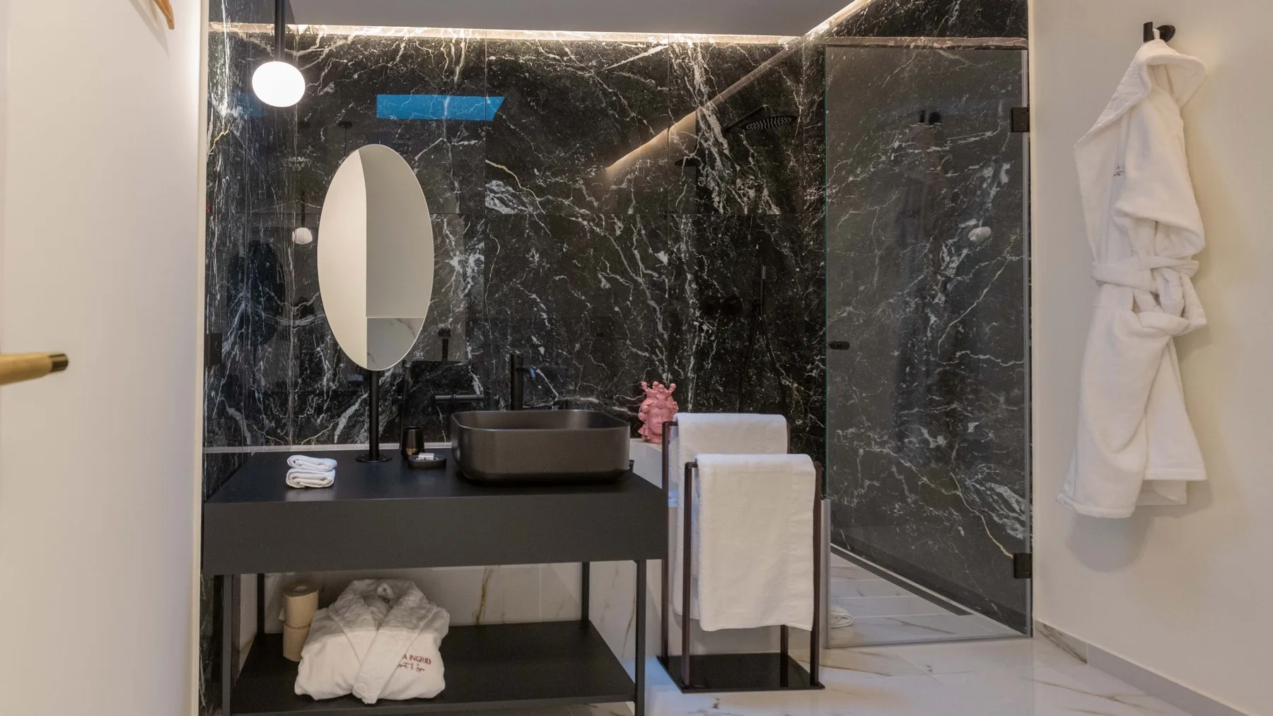 Un baño moderno con lavabo oscuro, espejo ovalado y ducha de cristal.