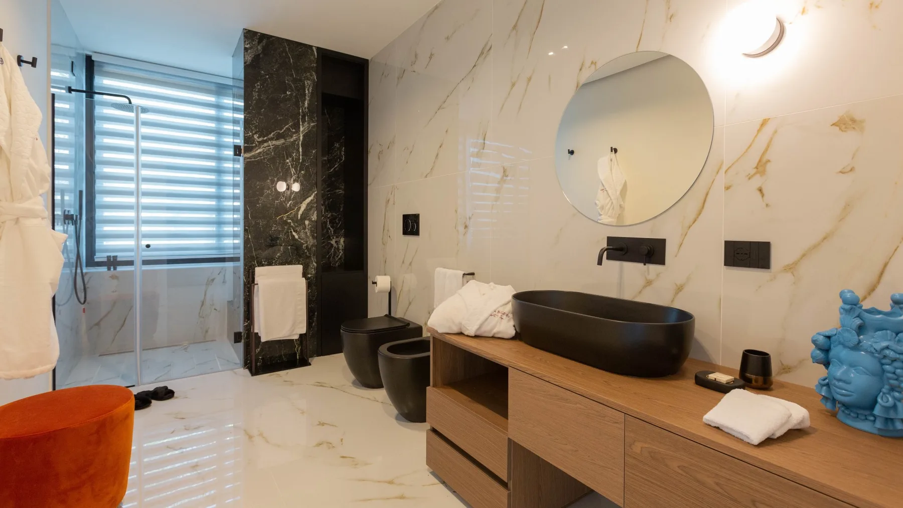 Un baño con un espejo redondo sobre un lavabo oscuro.