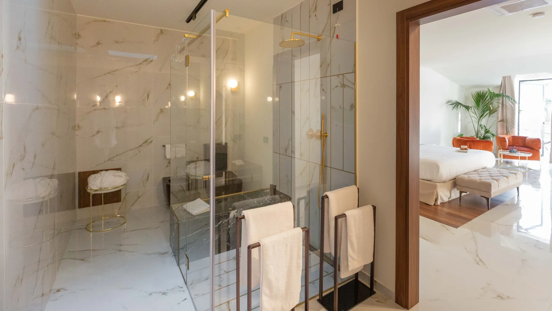 Un baño con ducha de cristal y toallas junto a una luminosa zona de estar.