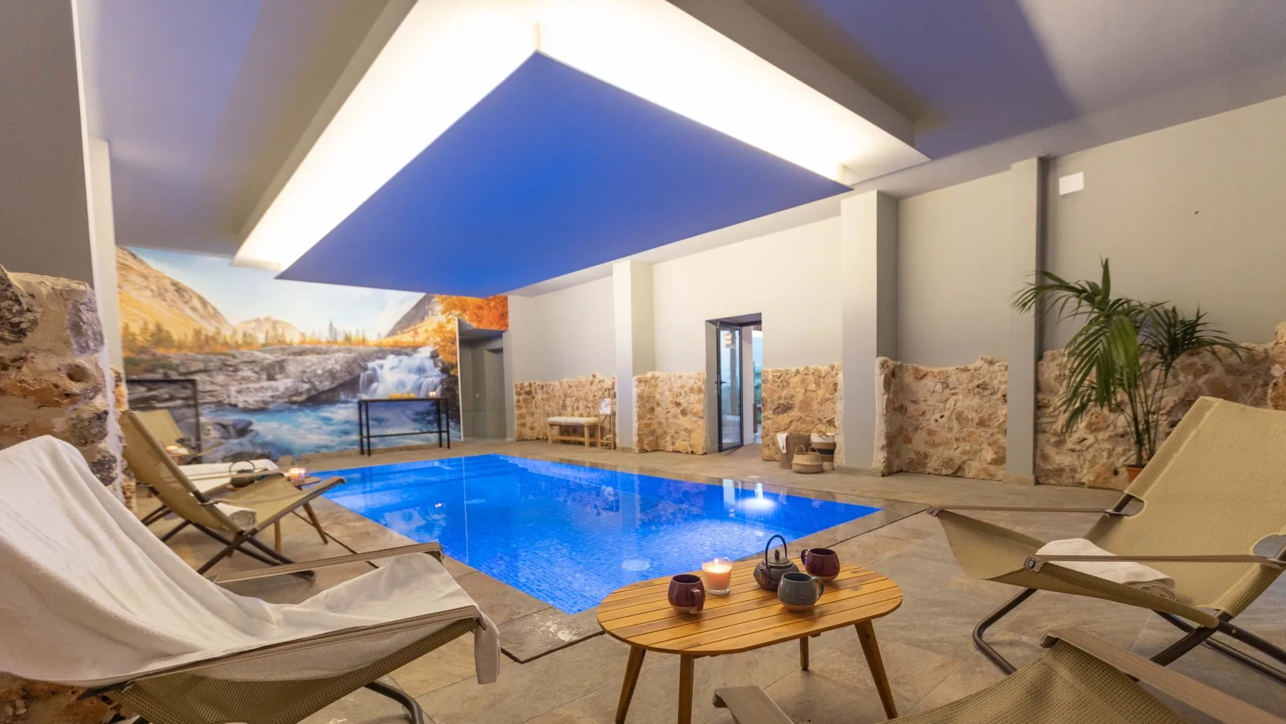 Una piscina cubierta está rodeada de asientos reclinables y paredes con diseño de piedra.