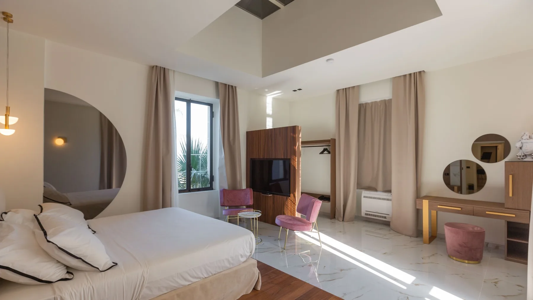 Un dormitorio luminoso con una cama grande, televisión y asientos junto a la ventana.