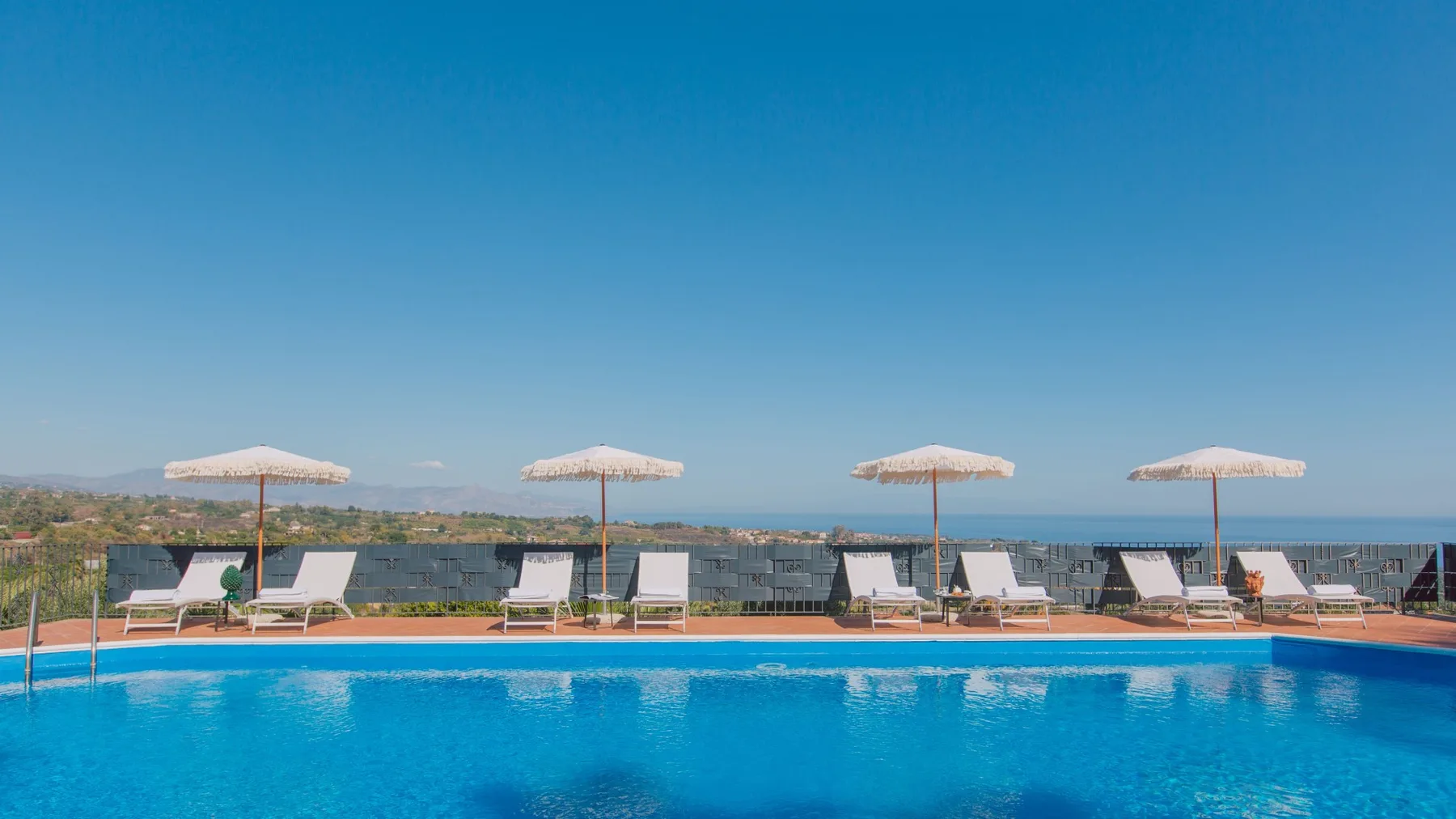 Una piscina mira hacia el mar, con tumbonas y sombrillas junto al borde.