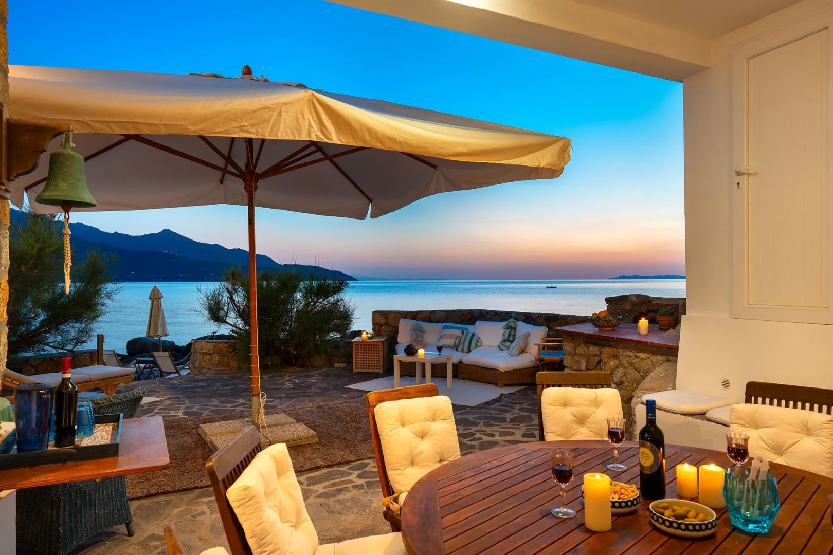 An outdoor terrace with seating and a large umbrella overlooks the water at sunset.