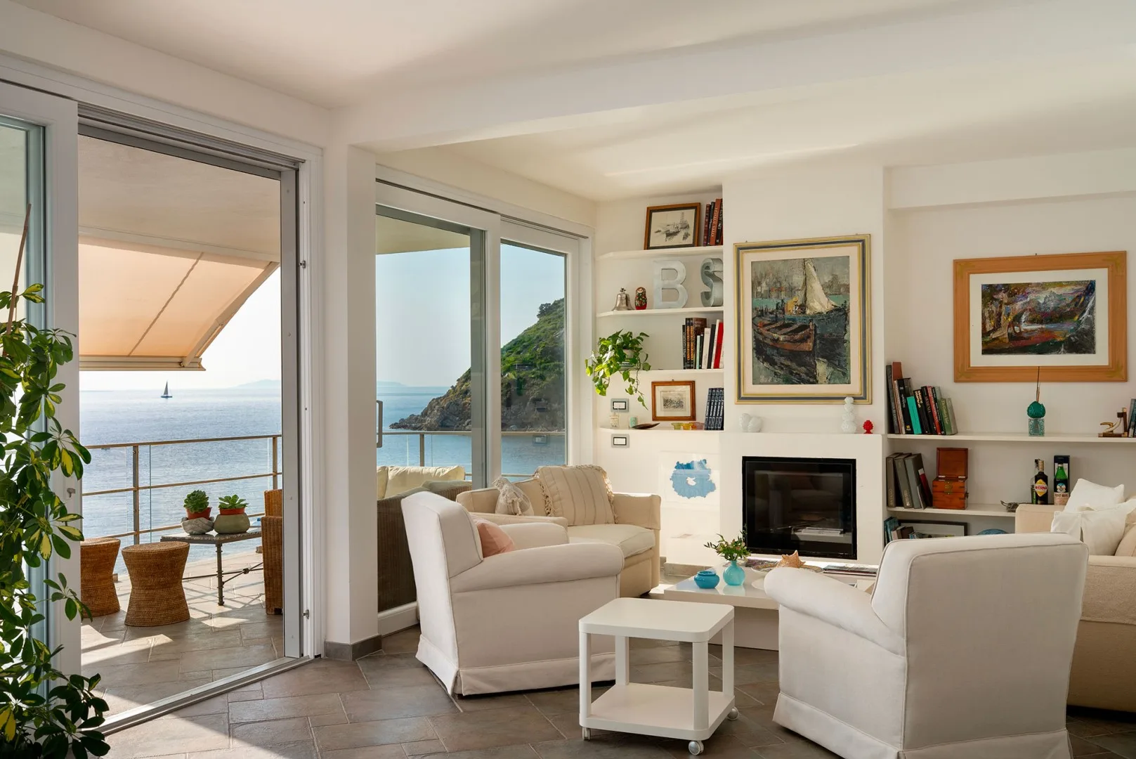 Bright living room with seating, a fireplace, and wide glass doors opening to a sea view.
