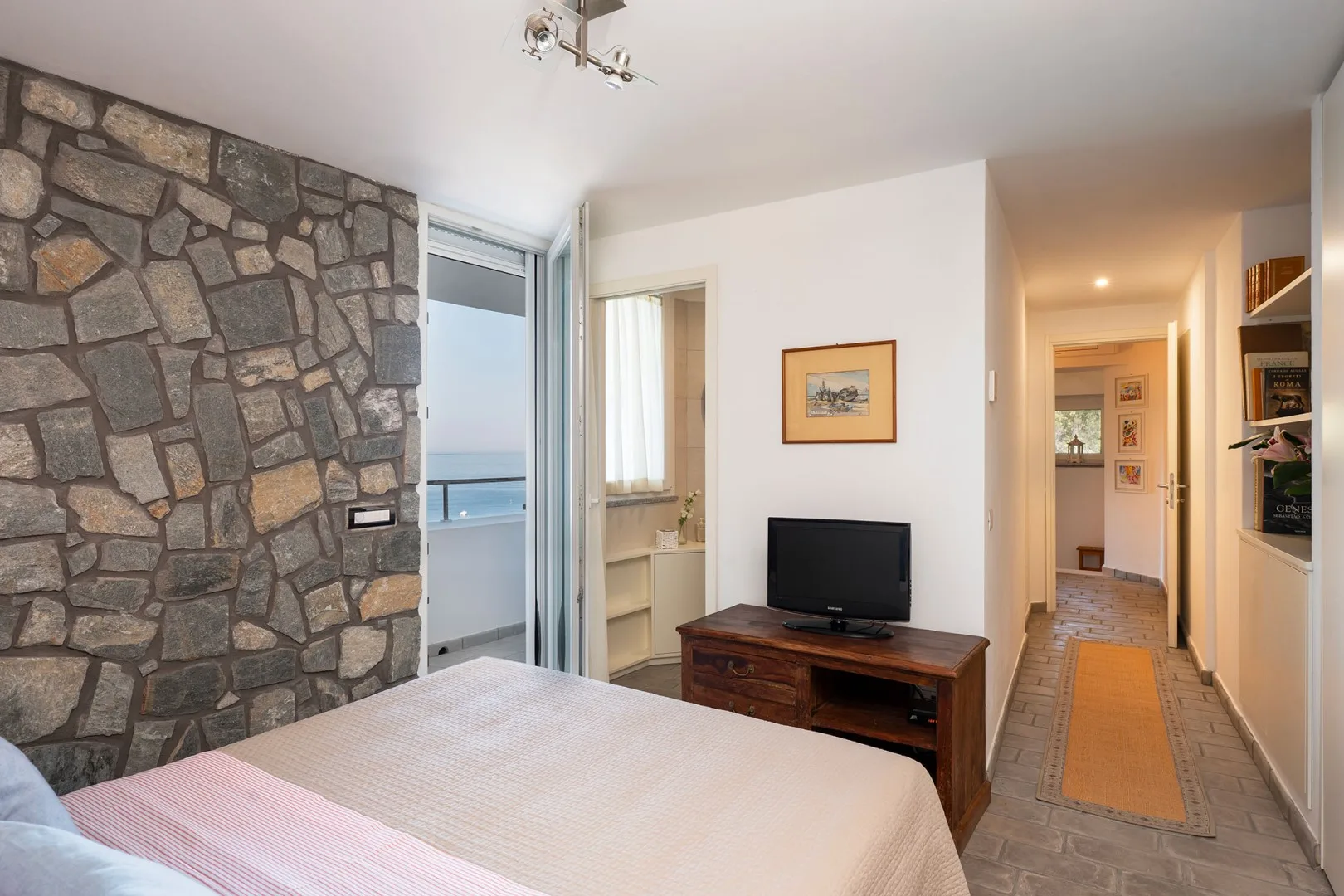 A bedroom with a television on a wooden stand beside a stone accent wall.