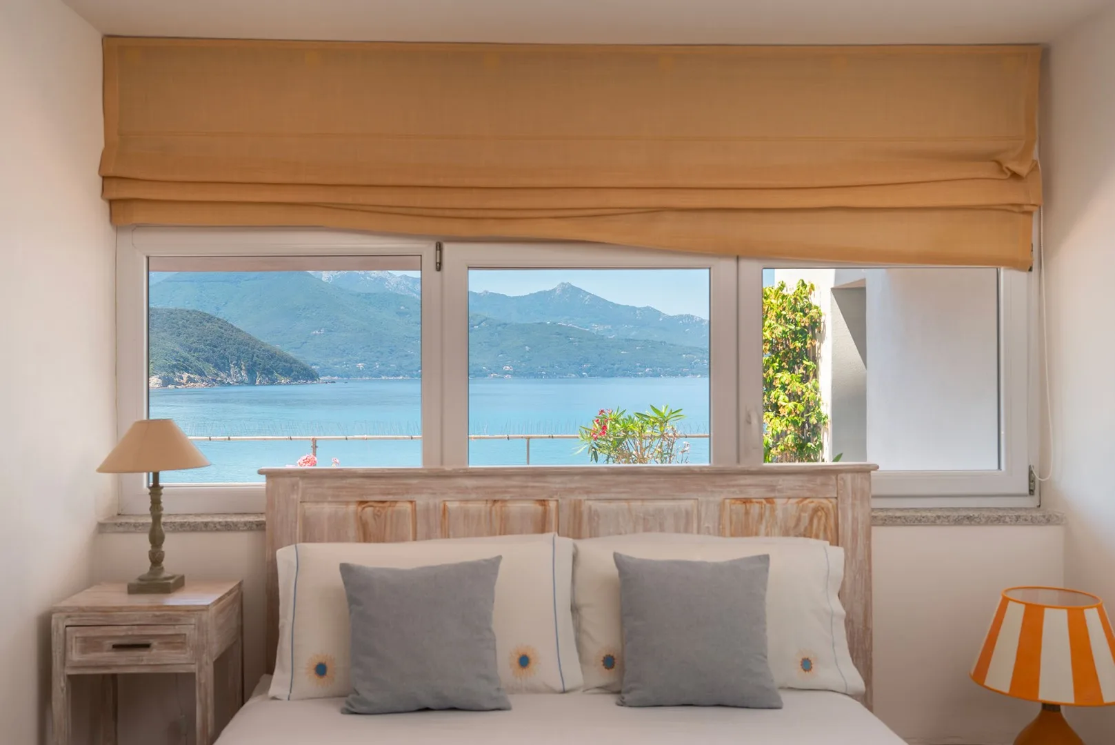 A bedroom with a bed facing a wide window overlooking the water and mountains.