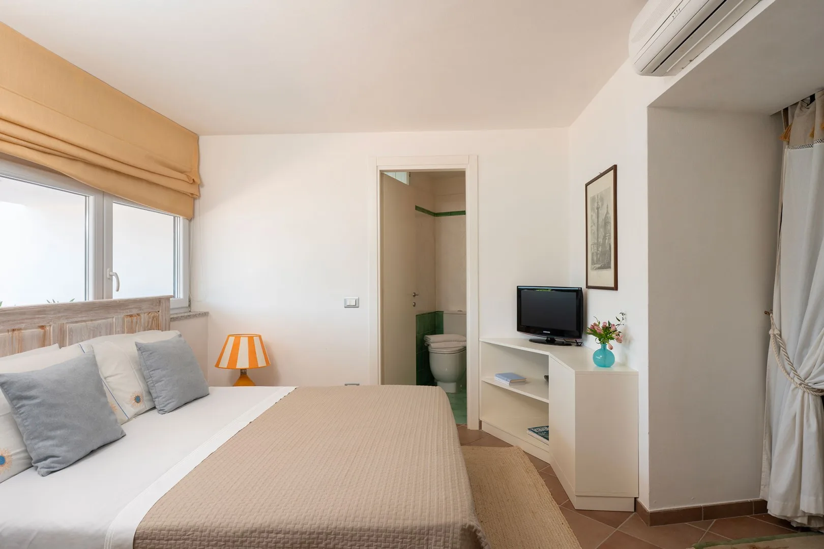 A bedroom with a bed beside a window and a television on a stand.