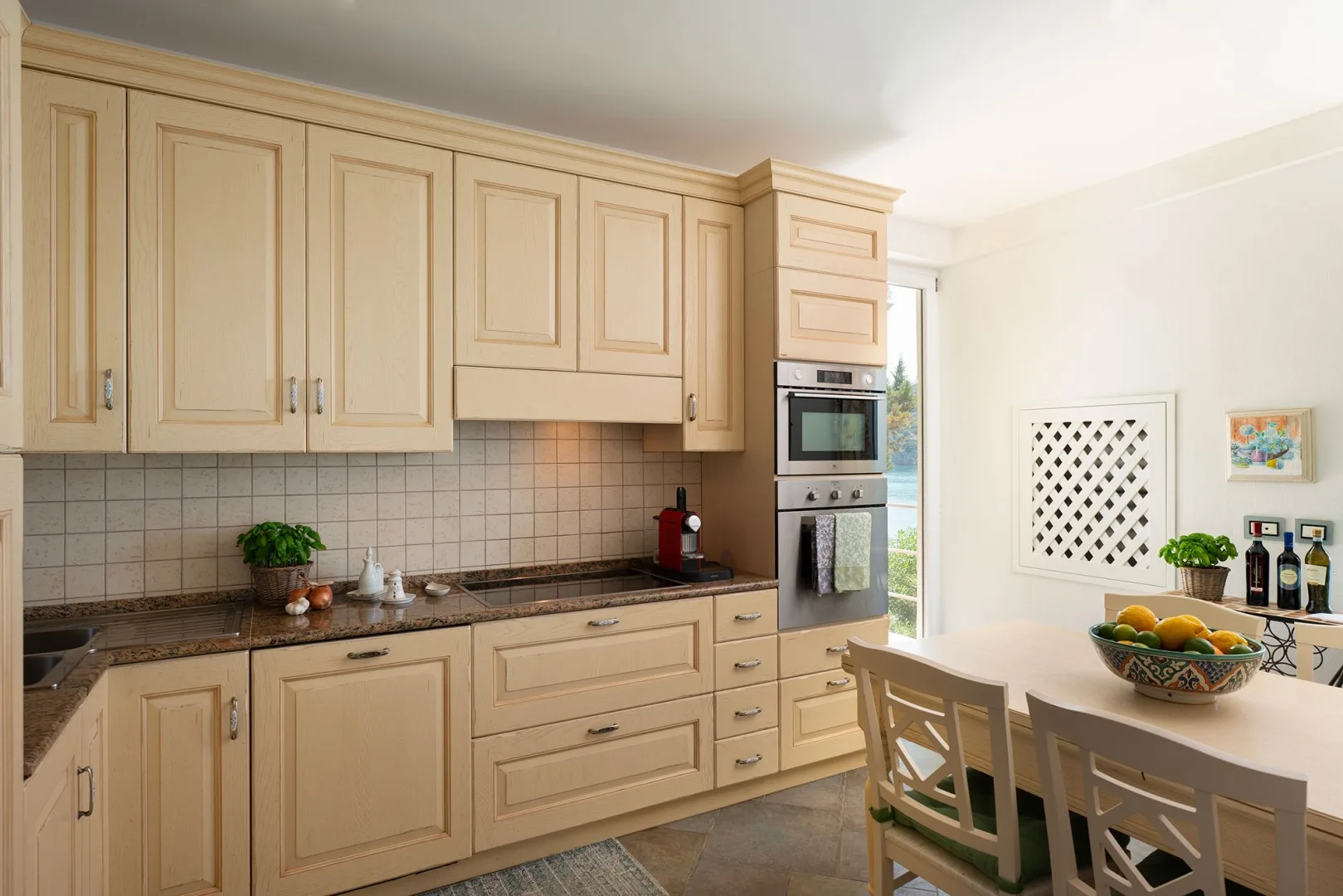 A bright kitchen with pale cabinets, a tiled backsplash, and a dining table.