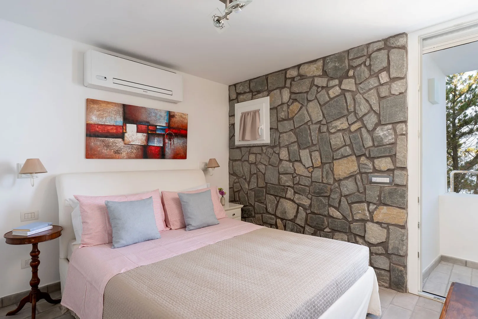 A bedroom with a bed, colorful wall art, and a stone accent wall.