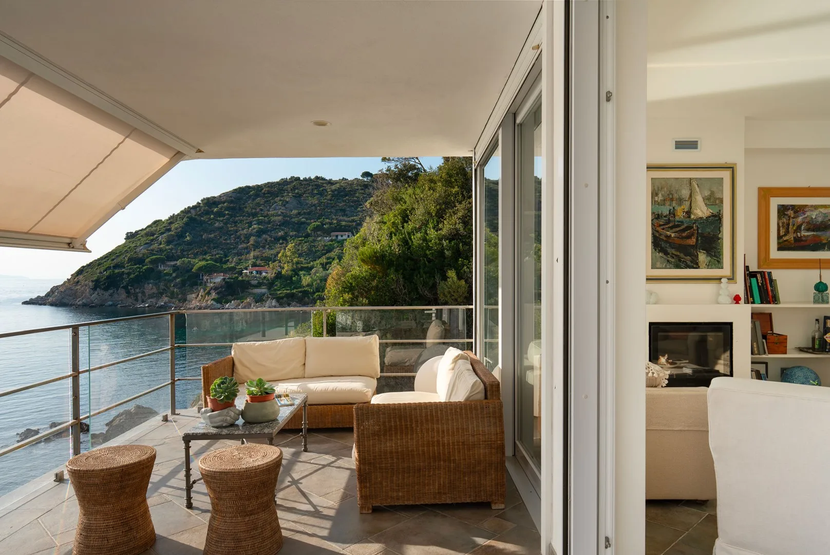 A coastal terrace with seating overlooks the water and a green hillside.