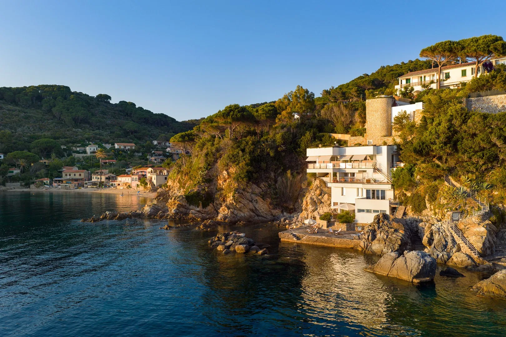 A coastal hillside with homes overlooking the water and rocky shoreline.