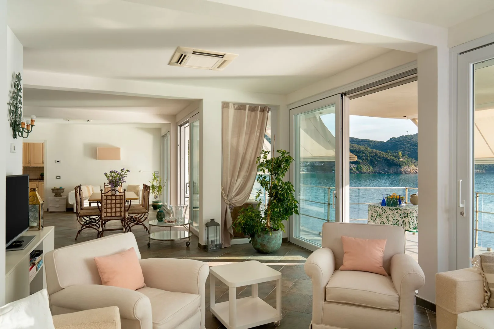 A bright living room opens onto a waterfront view through large glass doors.