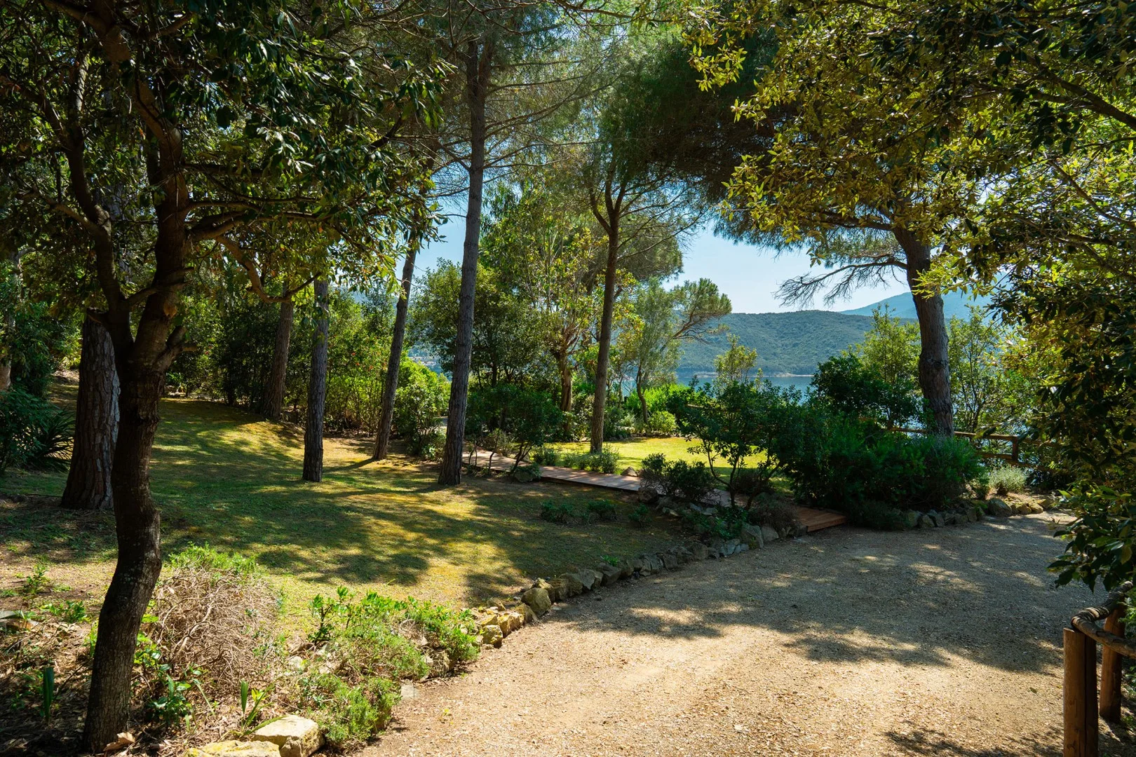 A shaded garden path winds between trees toward a view of the water.
