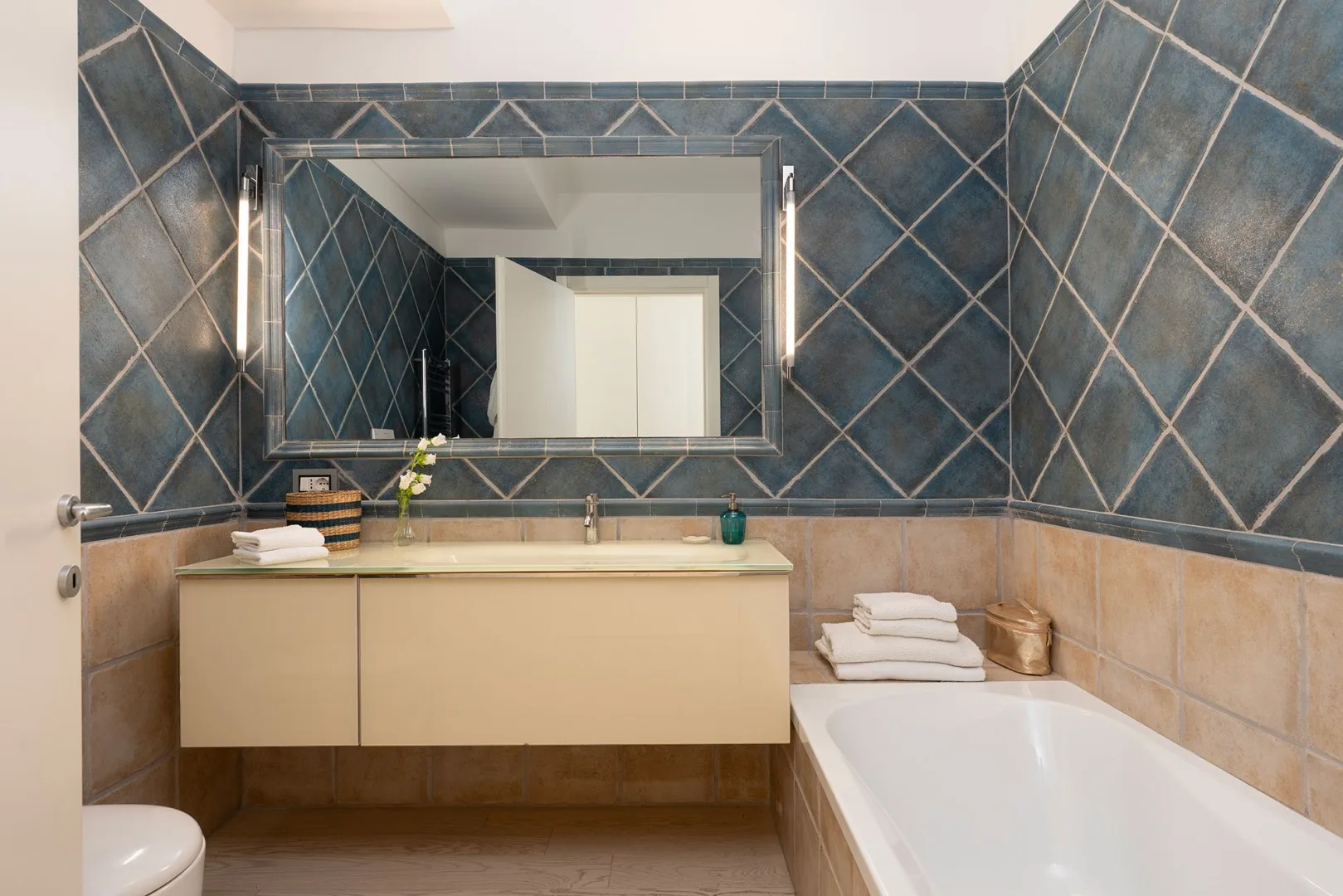 A tiled bathroom with a wide mirror, vanity, and bathtub.