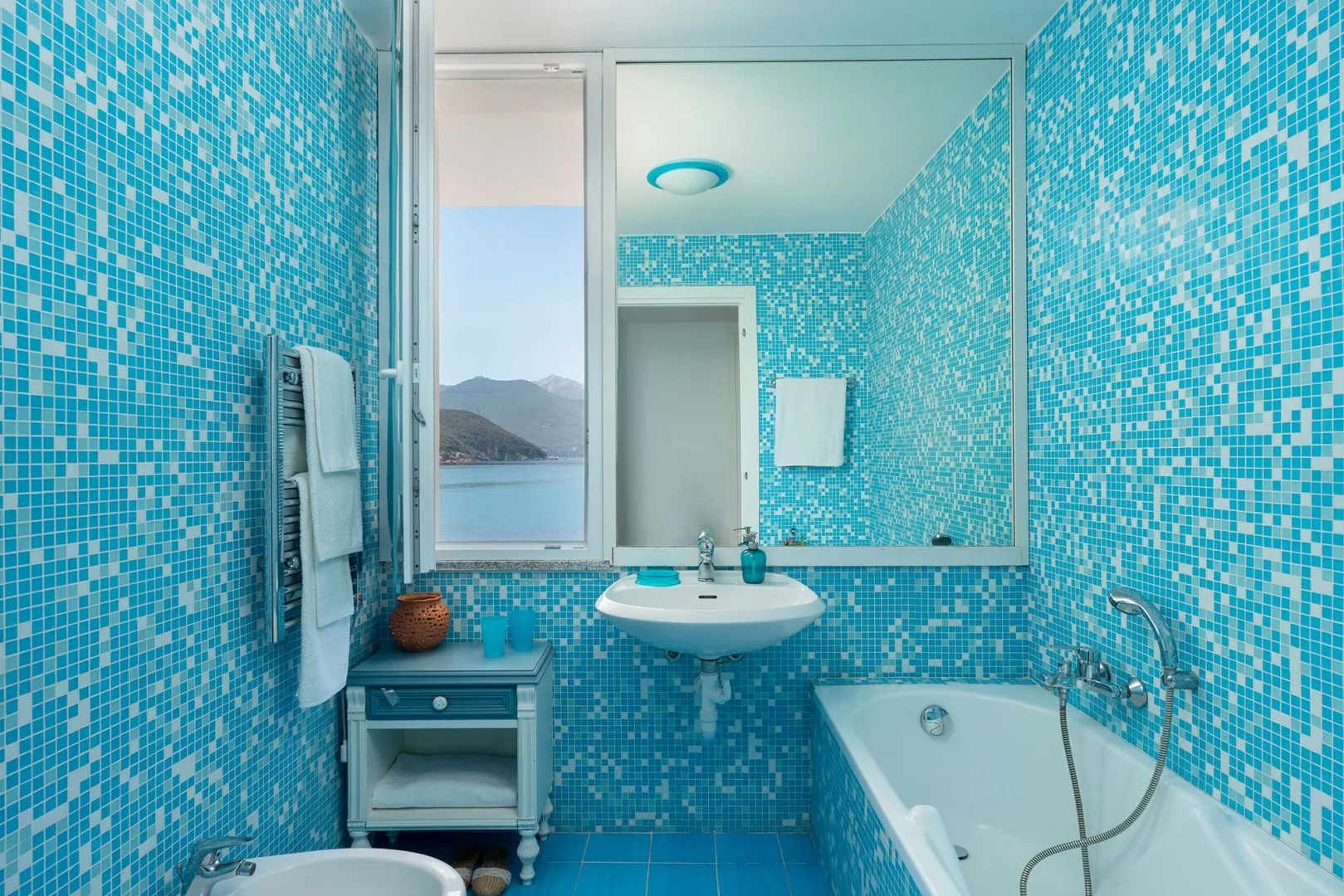 A tiled bathroom with a sink, bathtub, and a window overlooking the water.