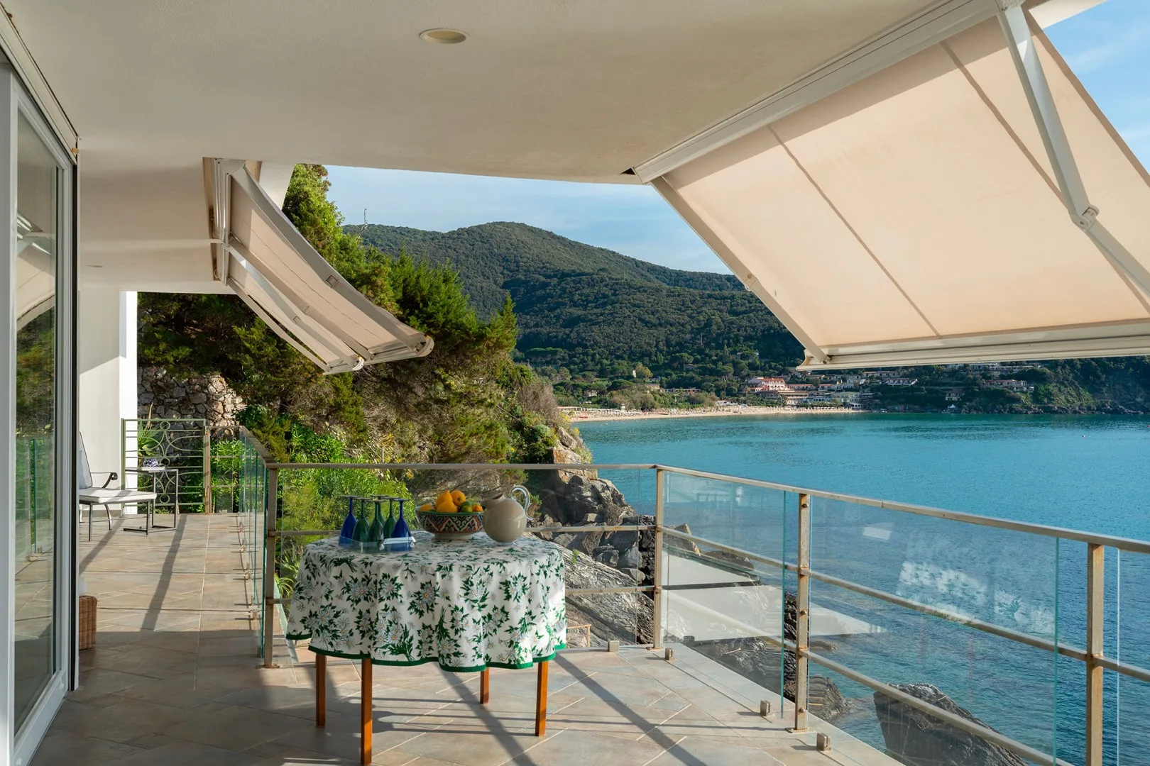 A seaside terrace overlooks blue water and a green hillside.