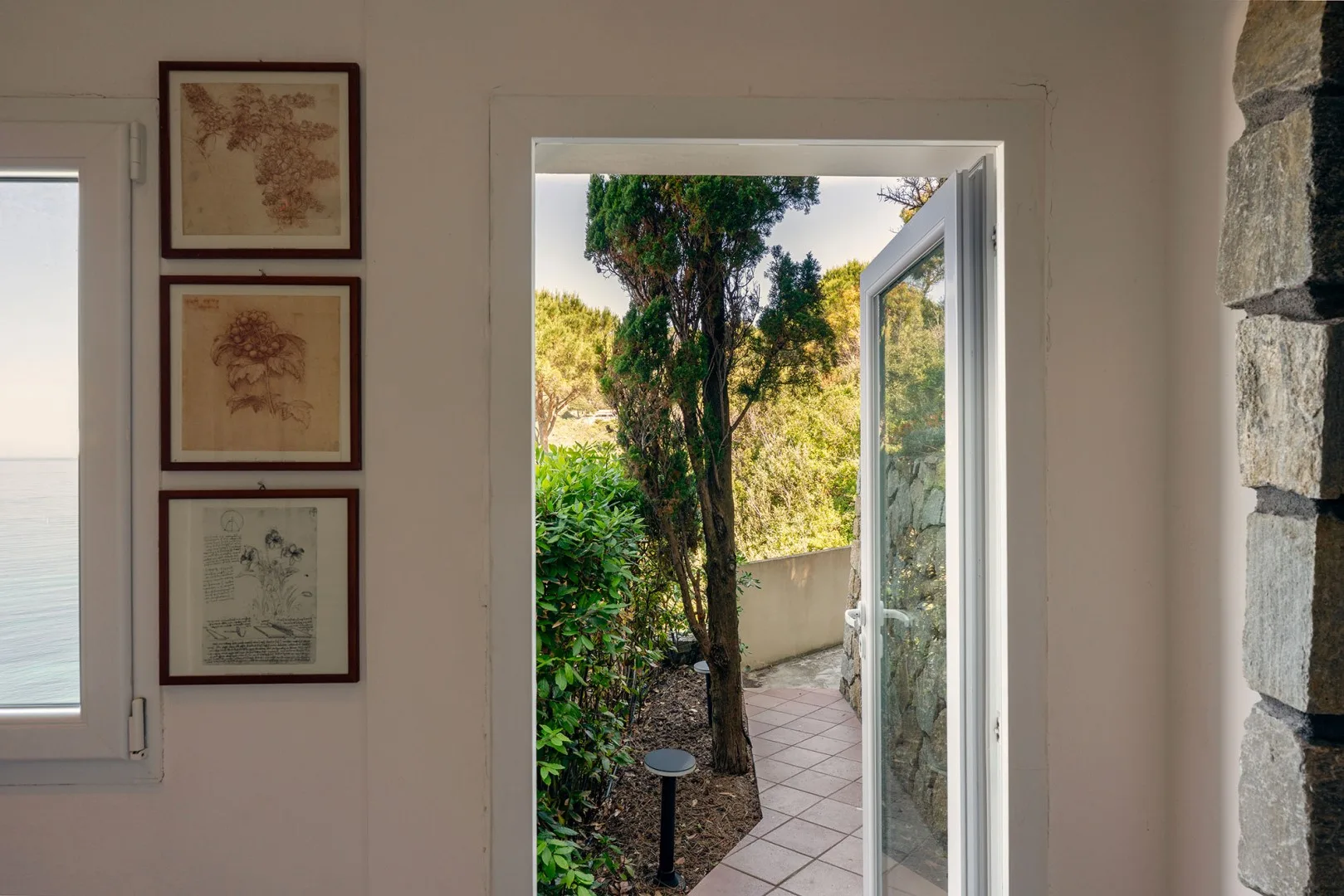A bright room opens onto a garden through an open glass door.