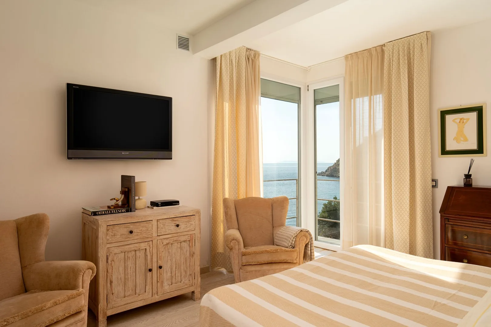 A bedroom with a bed, seating, and tall windows overlooking the sea.