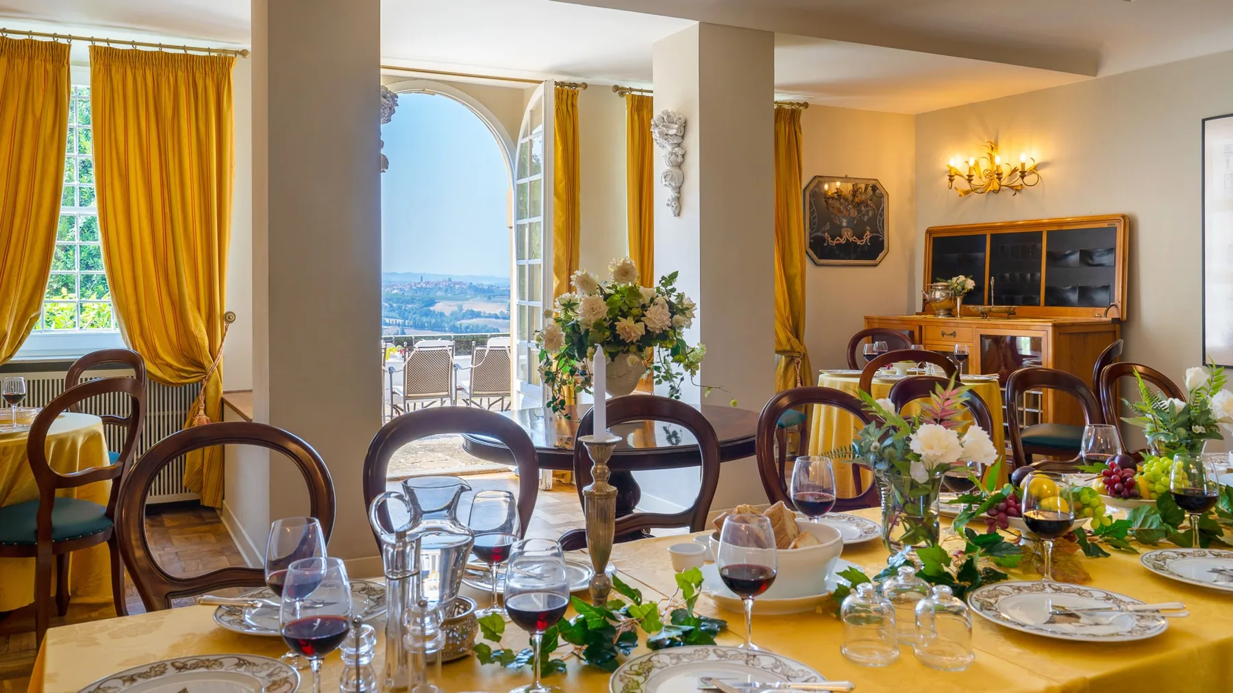Un comedor con una mesa puesta y ventanas altas con vista a un balcón.