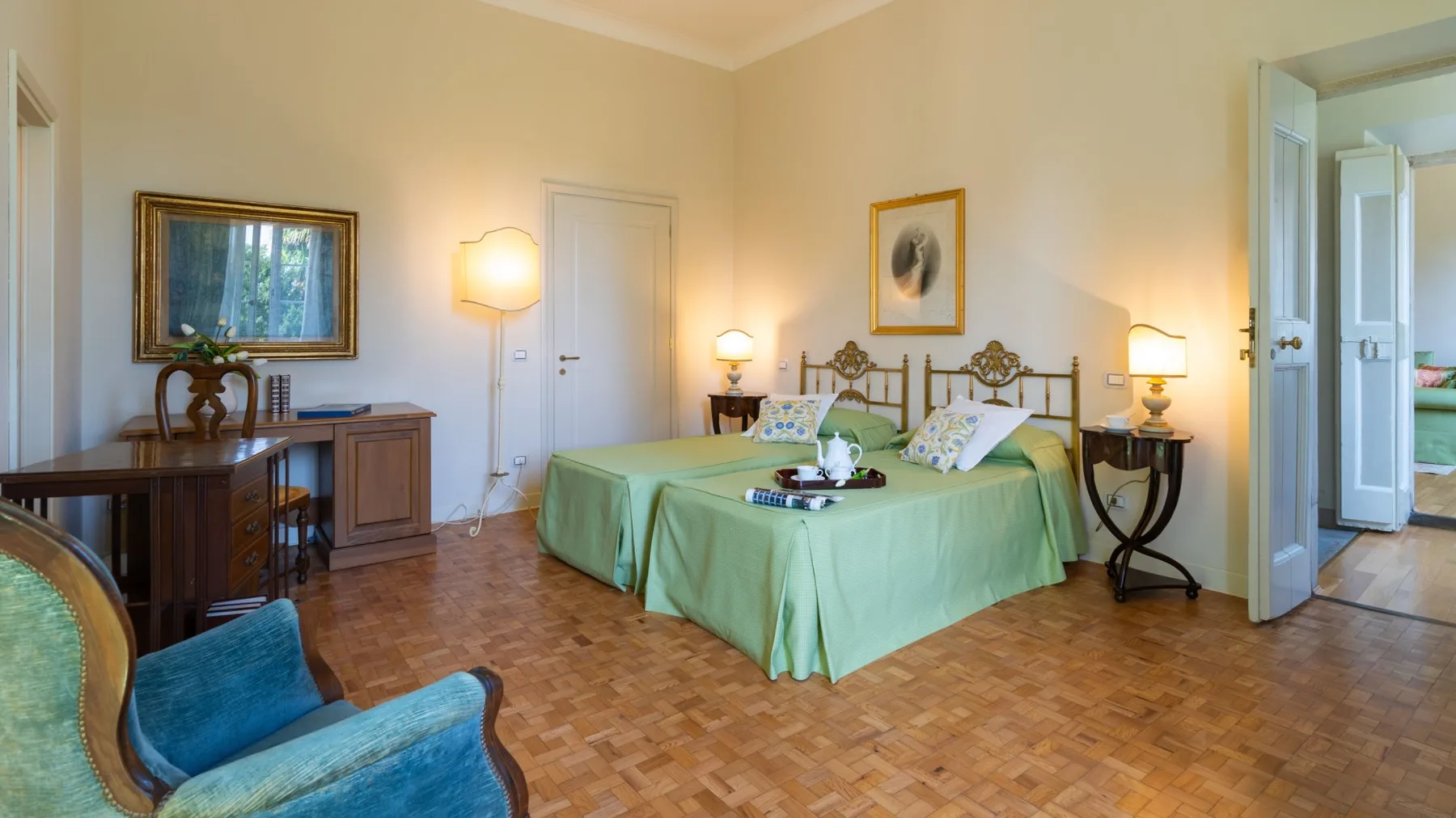Un dormitorio con una cama cubierta de verde, mesillas de noche y una silla tapizada azul.