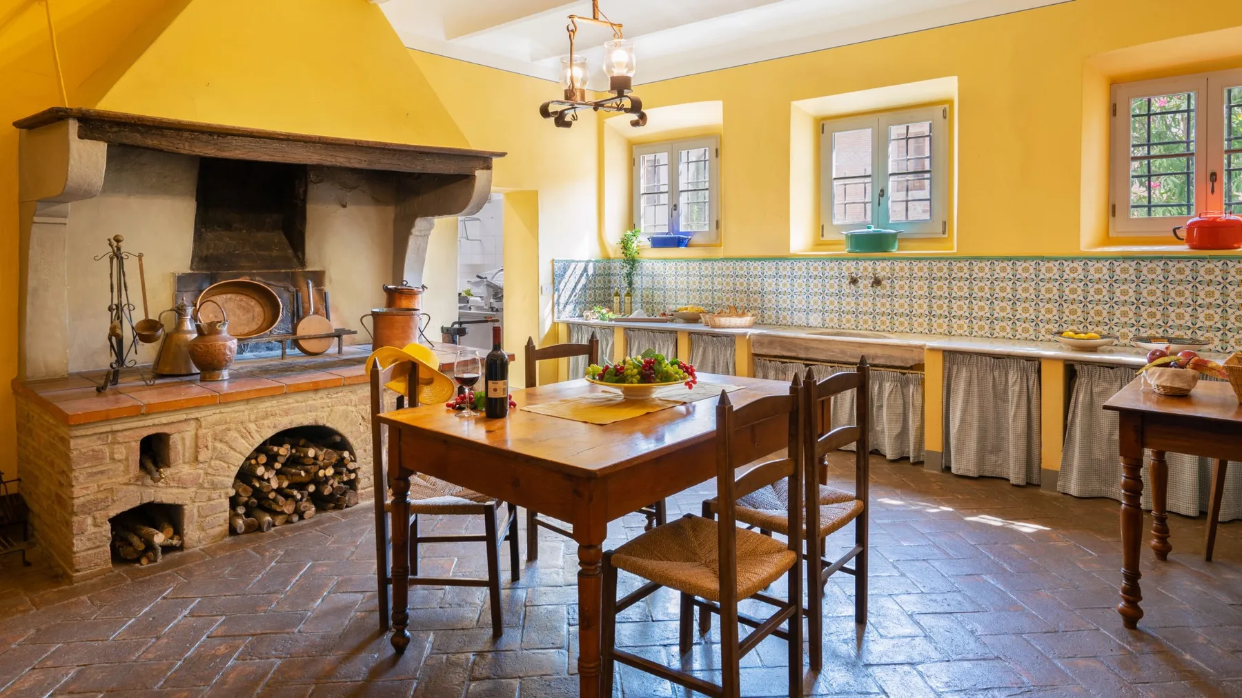 Una luminosa cocina y comedor amarillos con una gran chimenea y una mesa de madera.