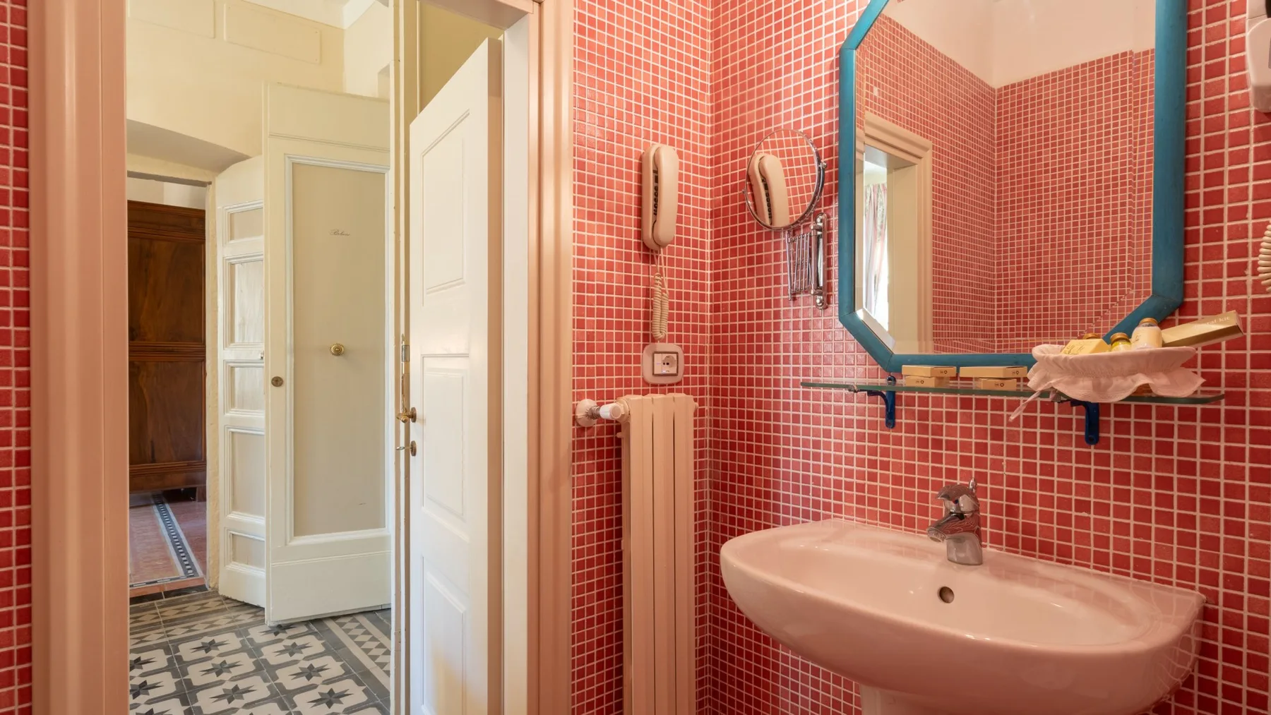 Un baño con azulejos, un espejo de pared y un lavabo rosa.
