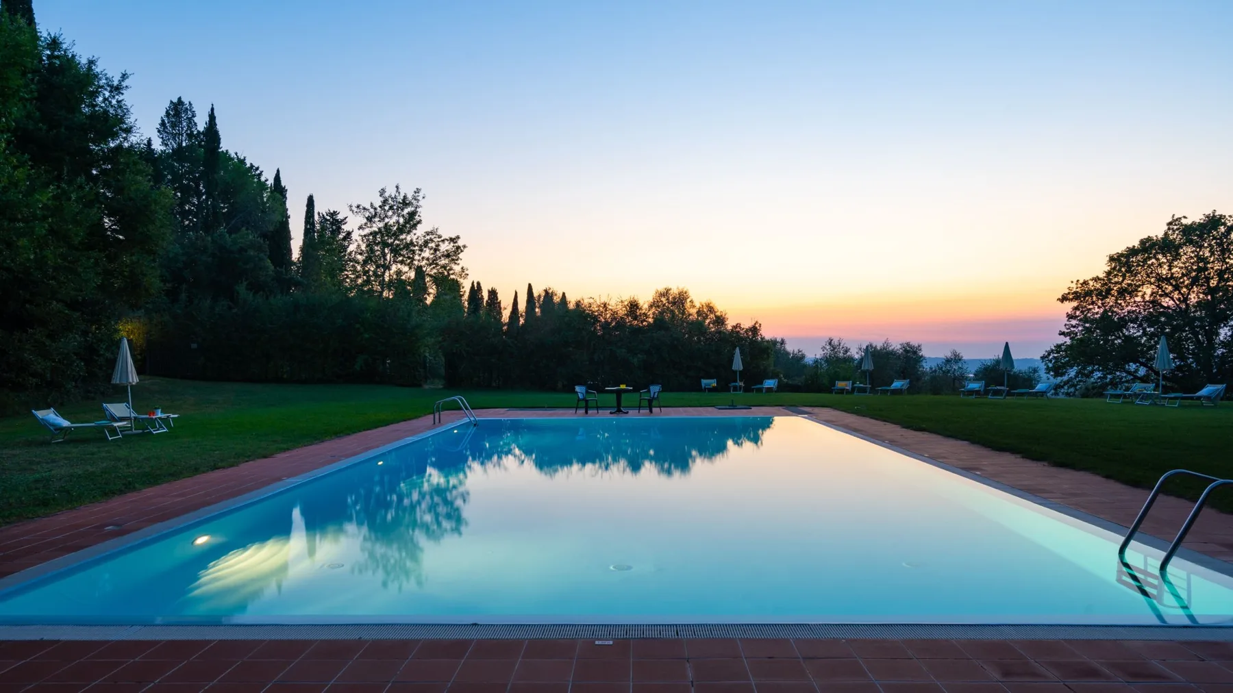 Una piscina al aire libre refleja el cielo colorido al atardecer.