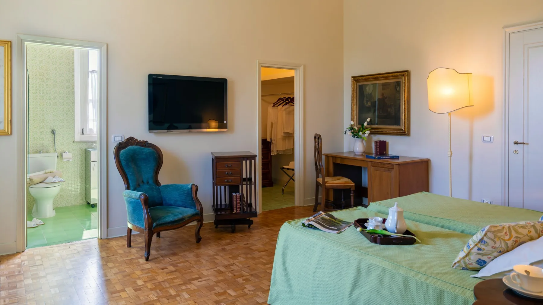 Un dormitorio con una cama cubierta de verde, un televisor y una puerta abierta hacia un baño.