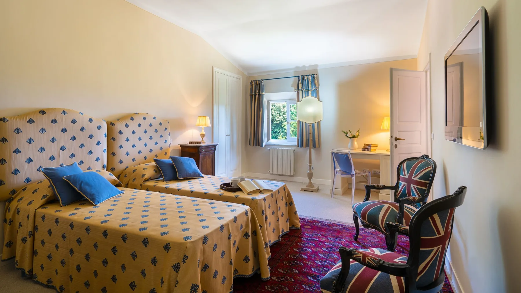 Un dormitorio con camas estampadas, un escritorio y sillones.