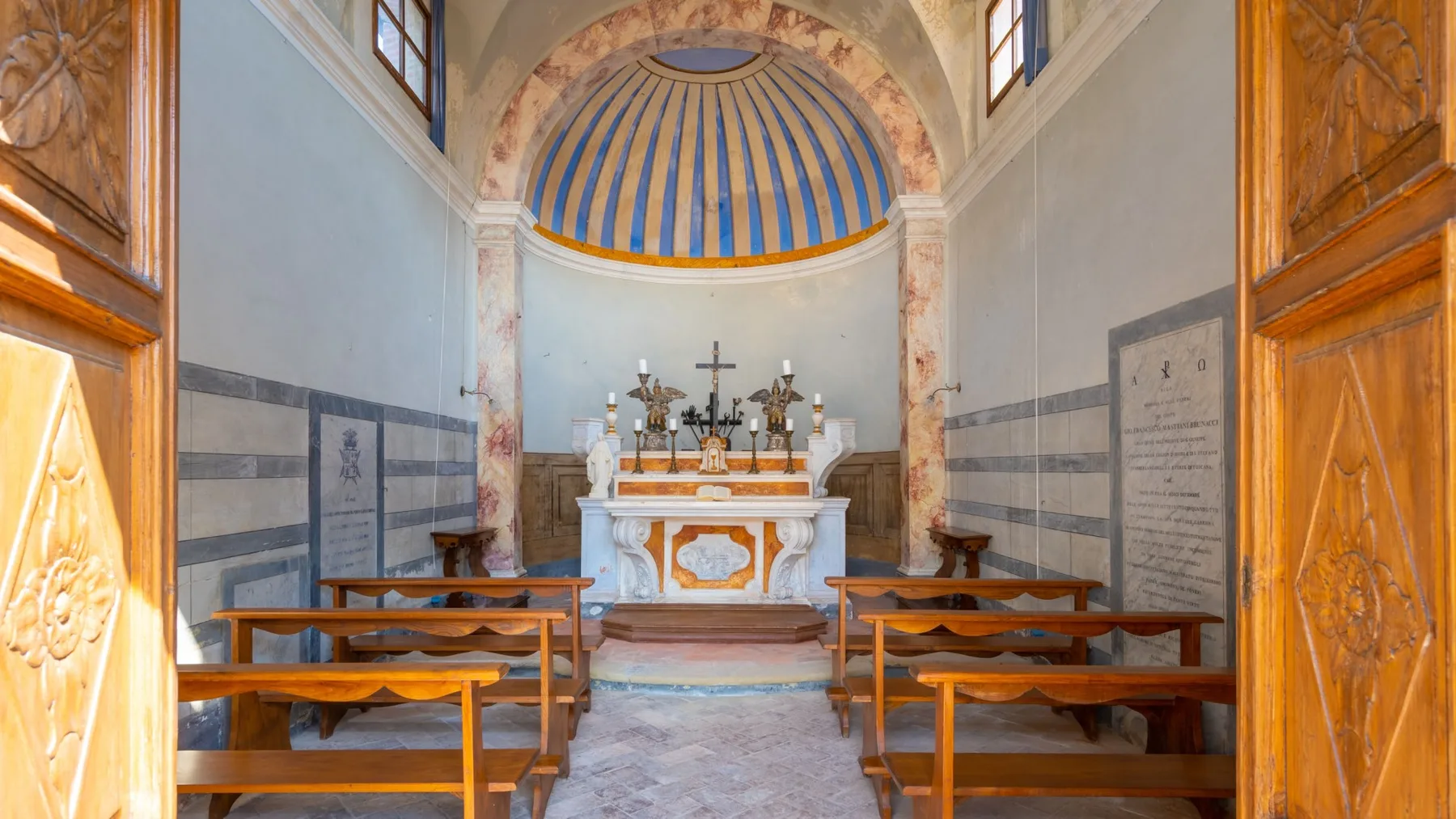Una pequeña capilla con bancos de madera frente a un altar bajo una cúpula de franjas azules.