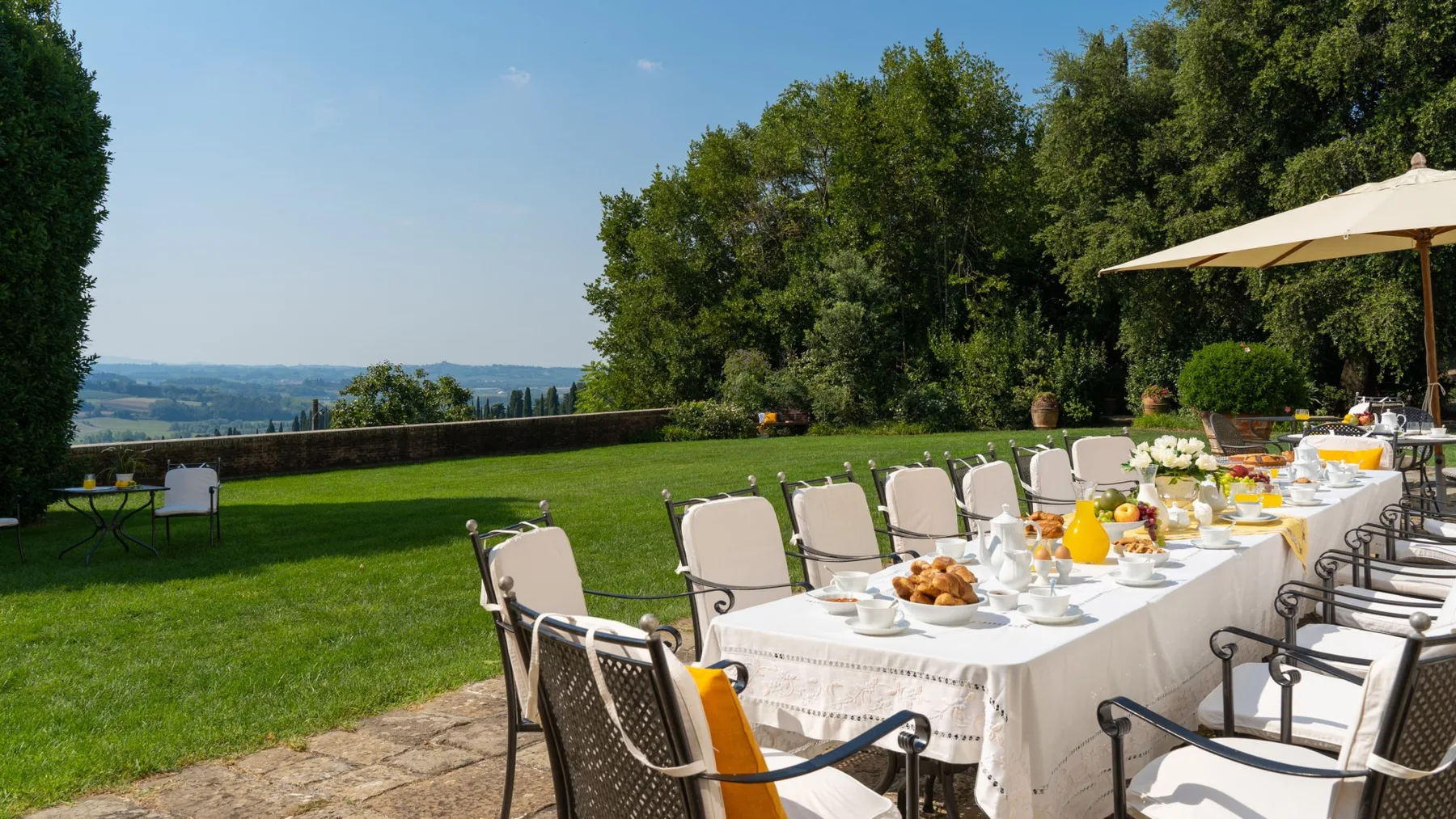 Un comedor al aire libre con una mesa larga en el césped junto a una vista arbolada.