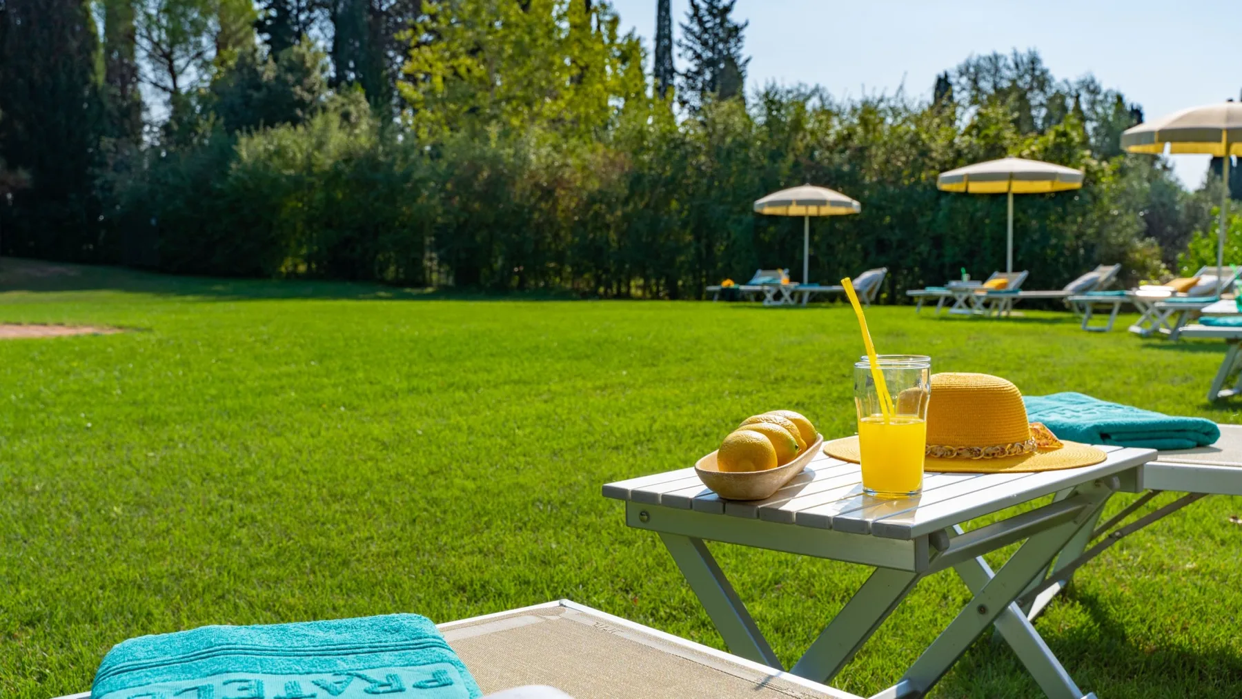 Una zona exterior junto a la piscina tiene tumbonas, sombrillas y una mesa pequeña con bebidas.