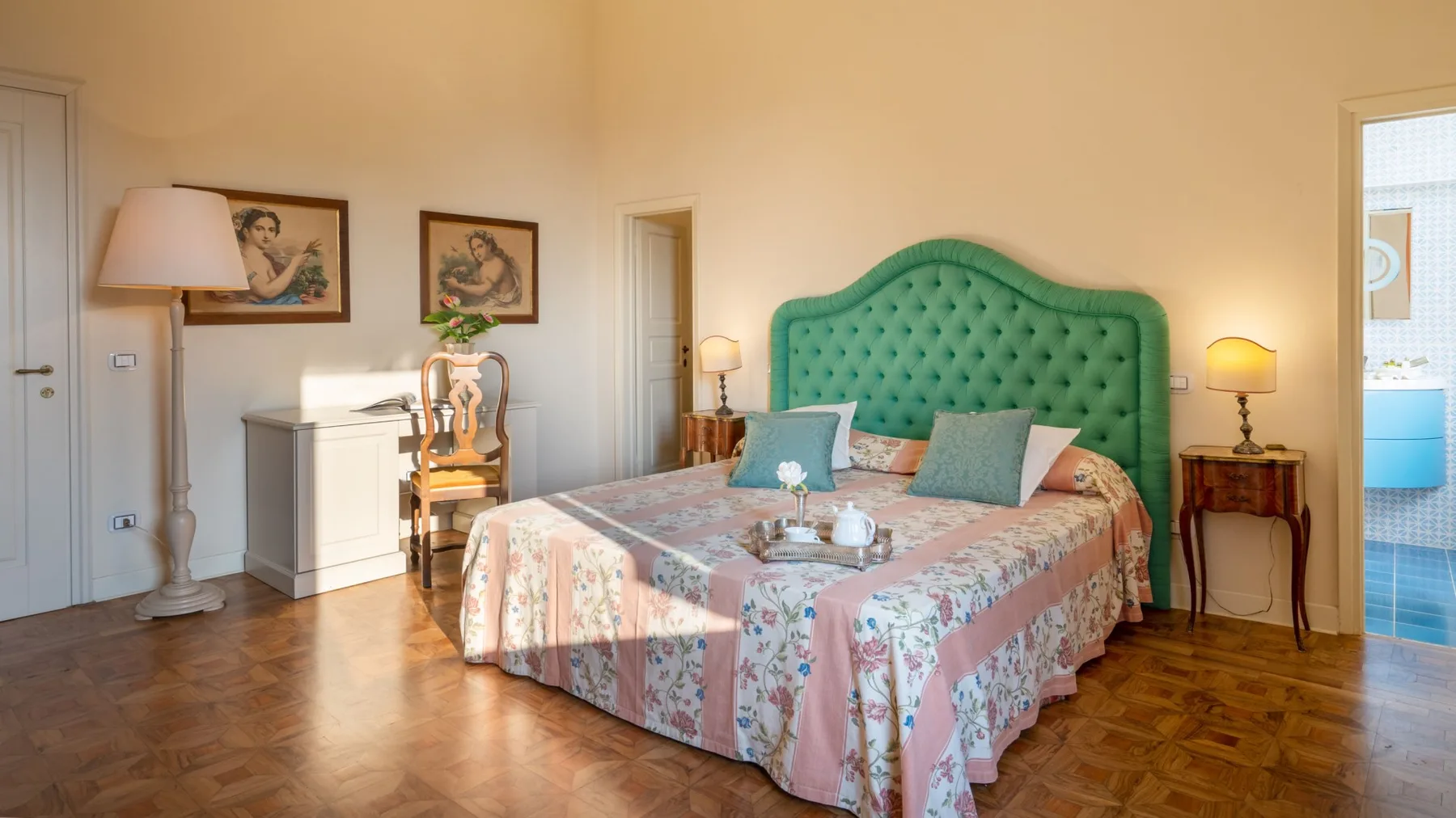 Un dormitorio con colcha floral, cabecero tapizado verde y lámparas de mesita.