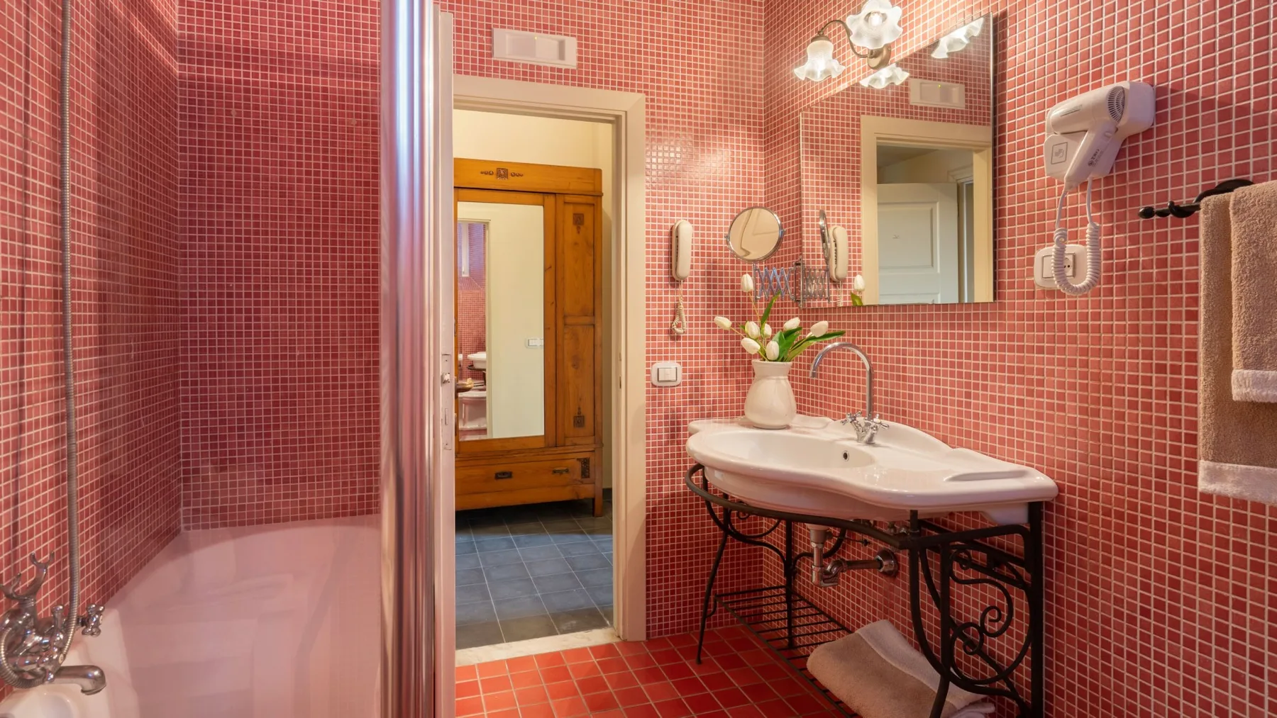 Un baño con azulejos rosados, lavabo y espejo junto a una ducha de vidrio.