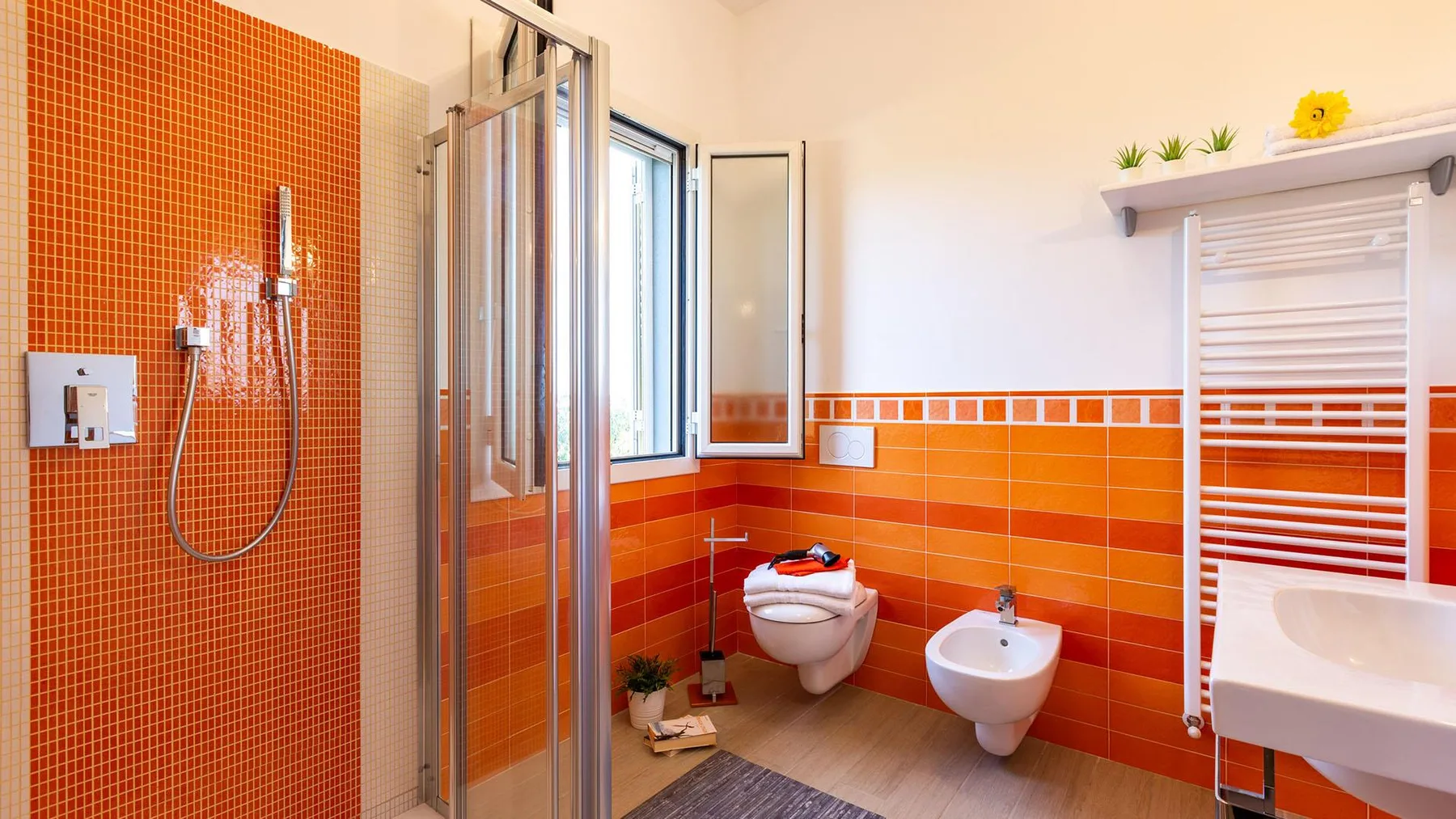 A bright bathroom with an orange tiled shower and white fixtures.