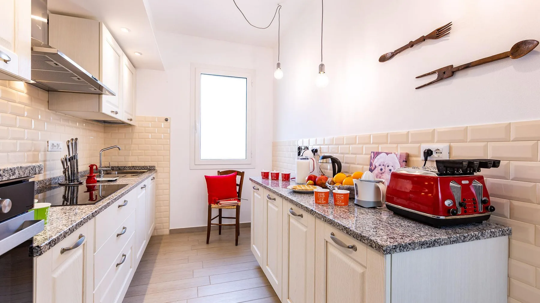 A bright kitchen with white cabinetry, stone counters, and a red toaster.